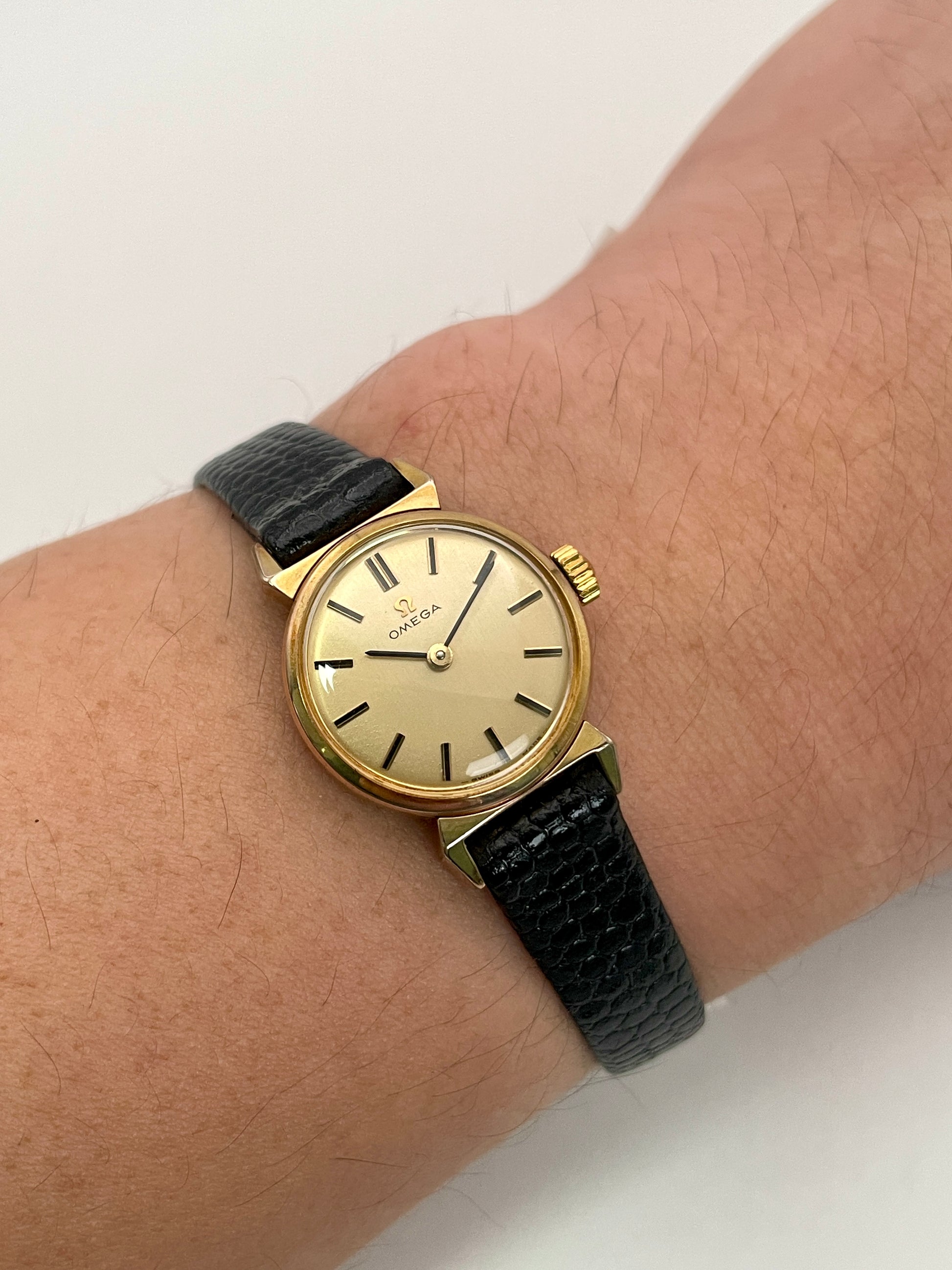 Omega Art Deco vintage ladies watch in gold worn on the wrist with black leather strap.