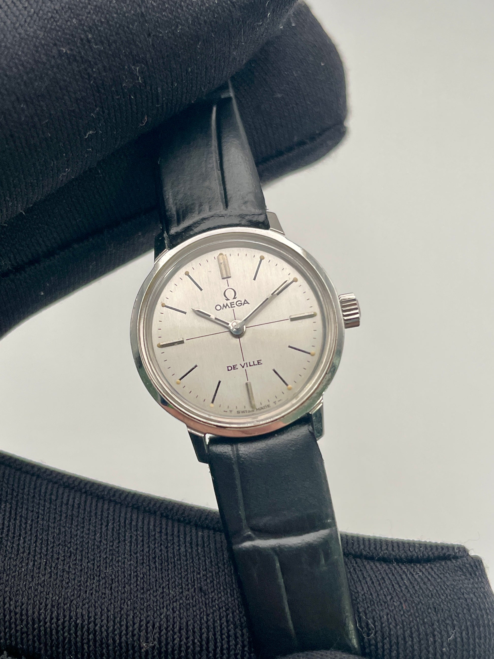 Close-up view of the Omega De Ville 515.007 vintage watch, highlighting its silver sunburst dial, minimalist markers, and sleek black strap.