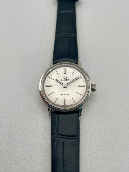Front view of the Omega De Ville 515.007 vintage women's watch in stainless steel, showcasing a silver sunburst dial with minimalist hour markers and a black leather strap.