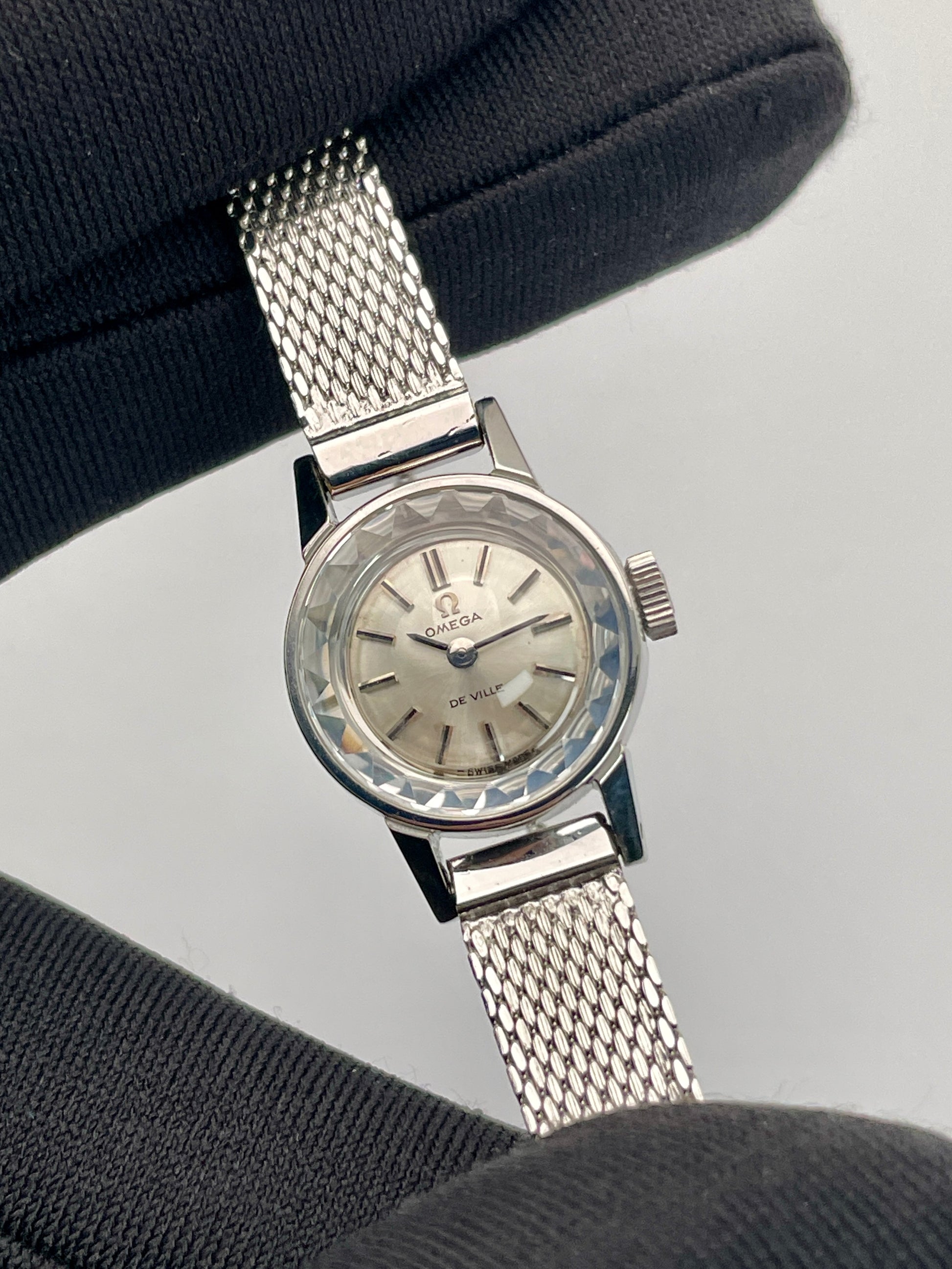 Close-up view of the Omega De Ville watch, focusing on the cut glass crystal and silver dial