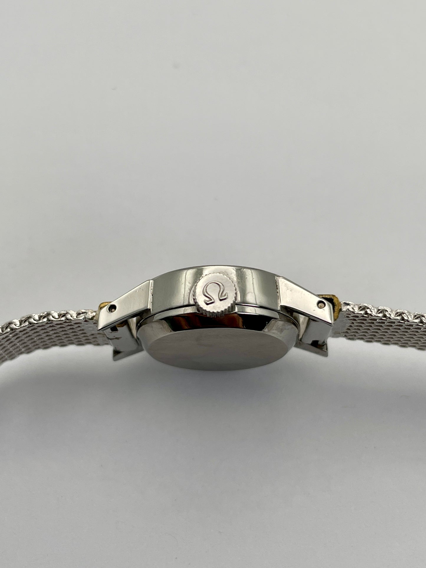 Close-up of the Omega De Ville watch crown, featuring the Omega signed crown and mesh bracelet