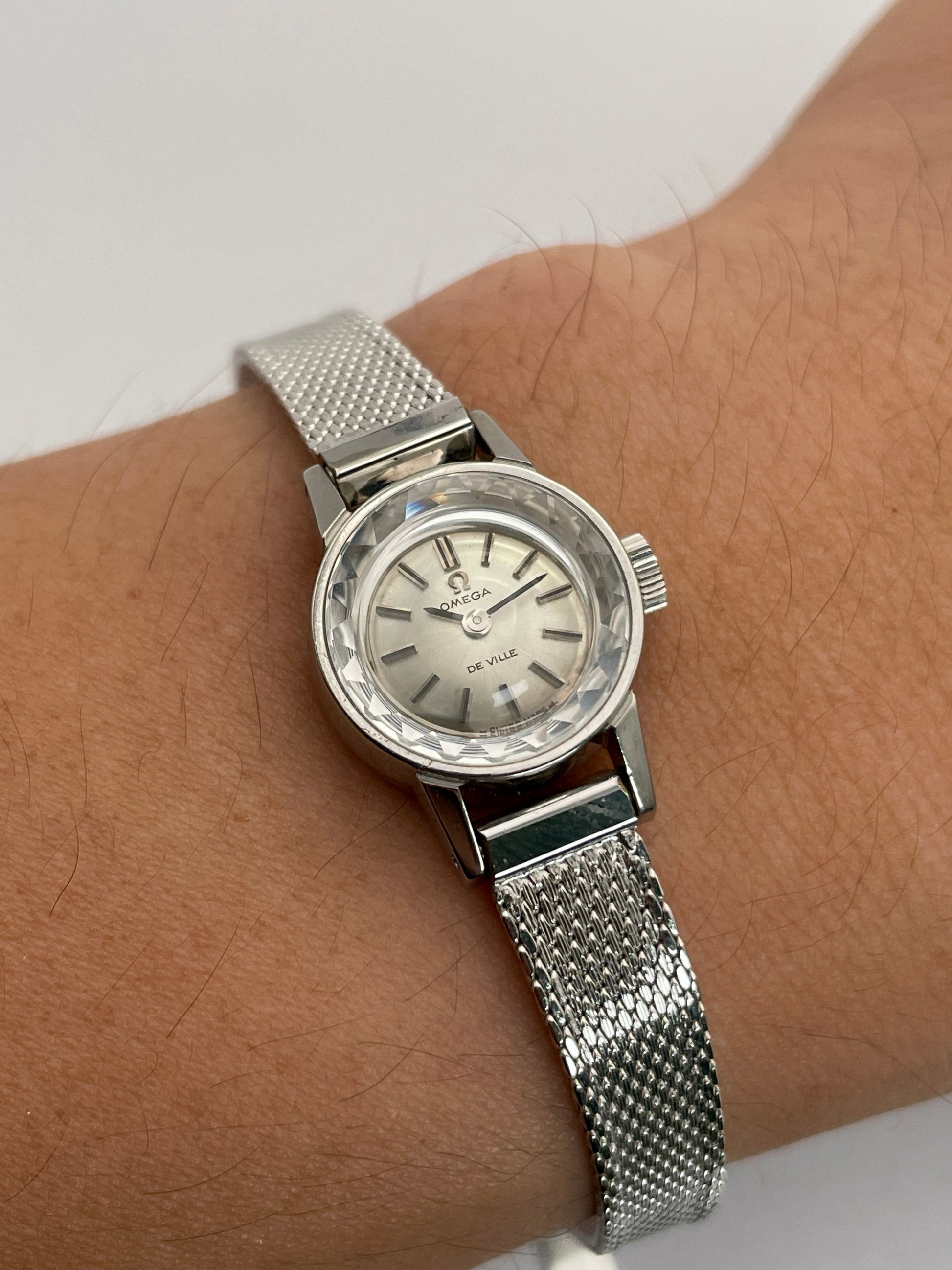 Wrist shot of the Omega De Ville watch with cut glass crystal, stainless steel case, and mesh bracelet