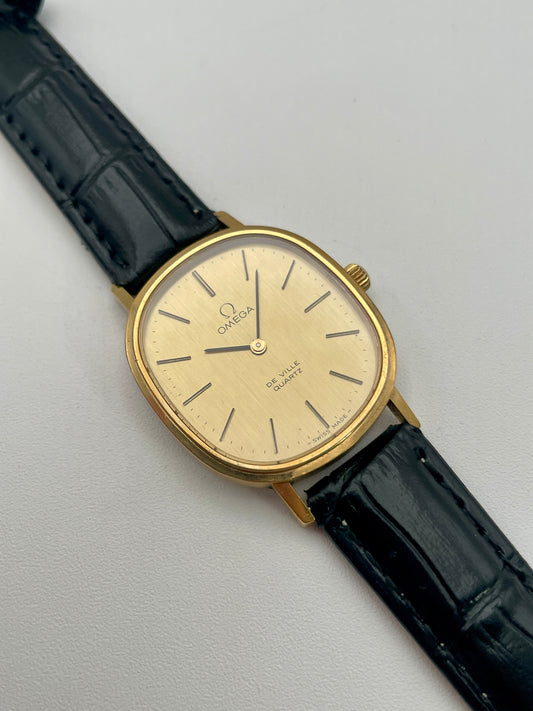 Omega De Ville Oval watch in gold with a champagne dial and black leather strap, main view.