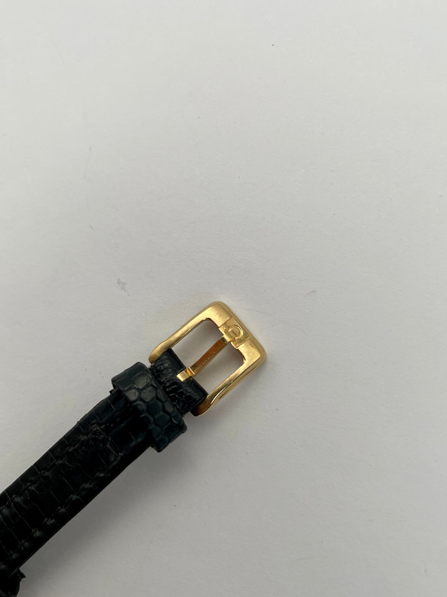 Close-up view of the buckle on Omega De Ville vintage gold watch with a black leather strap.