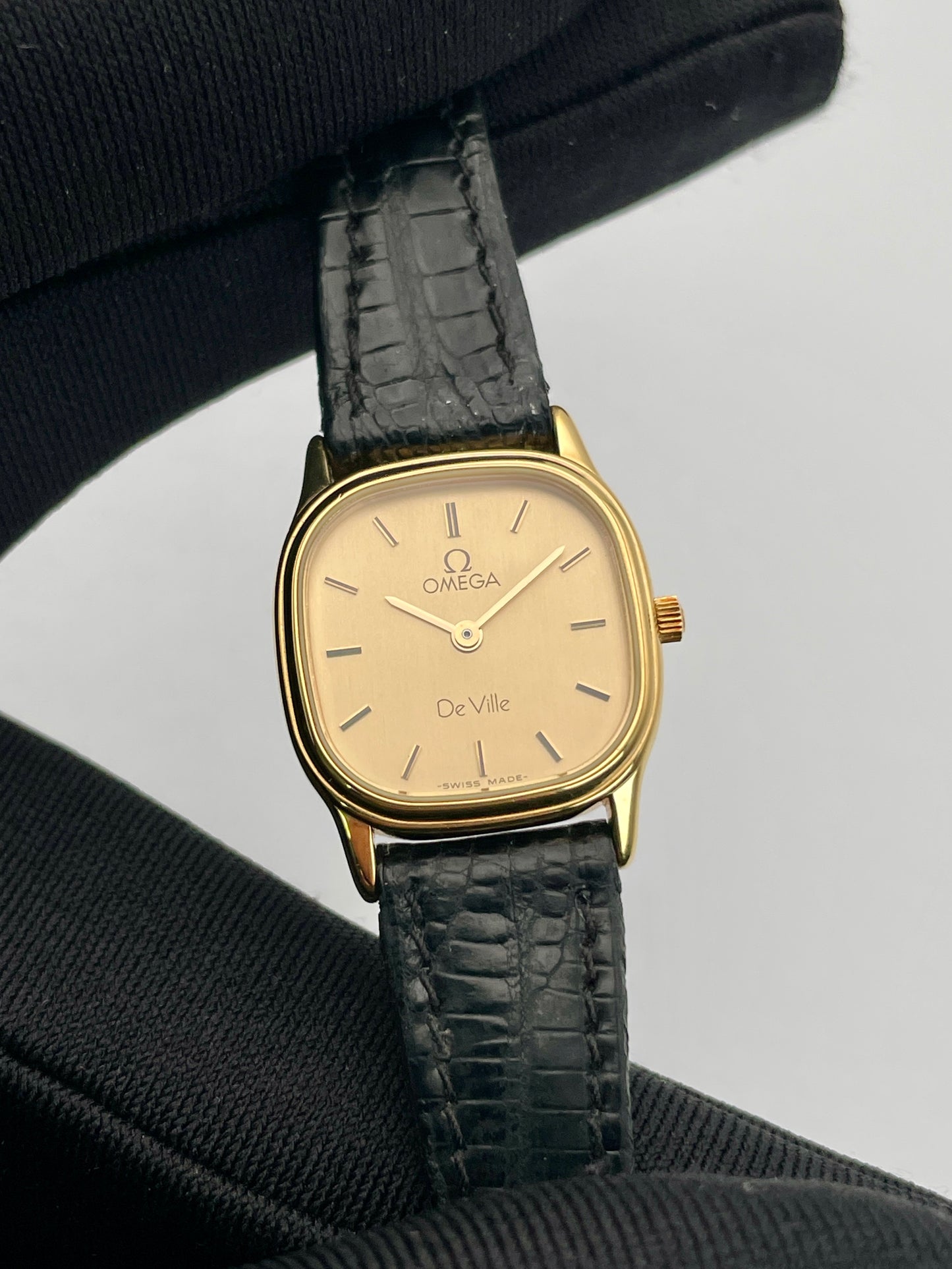 Close-up of Omega De Ville vintage gold watch showcasing the champagne dial and gold square case with black leather strap.