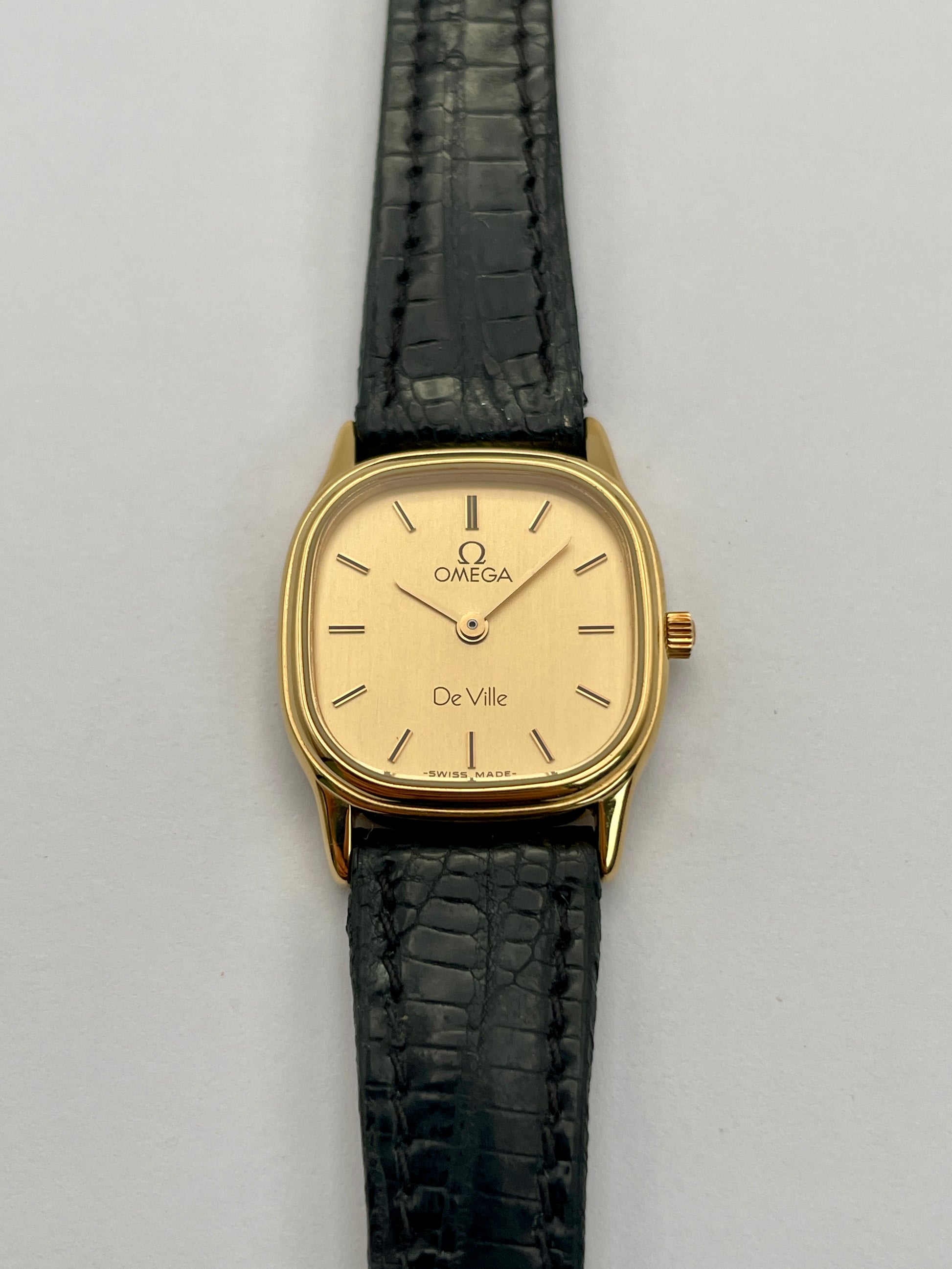 Front view of Omega De Ville vintage gold watch with a square case, champagne dial, and black leather strap.