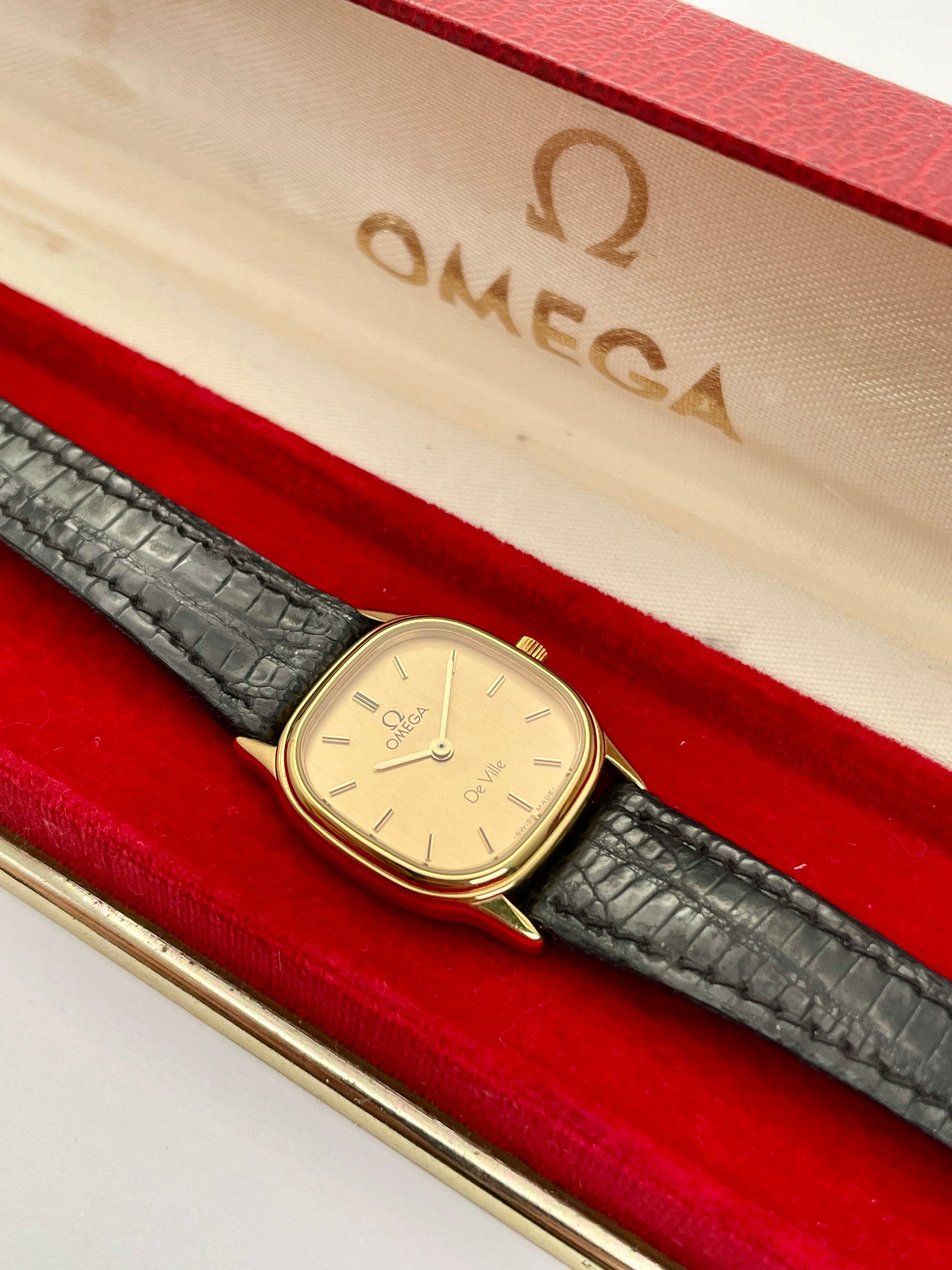 Omega De Ville vintage gold watch with a square case, champagne dial, and black leather strap, in box