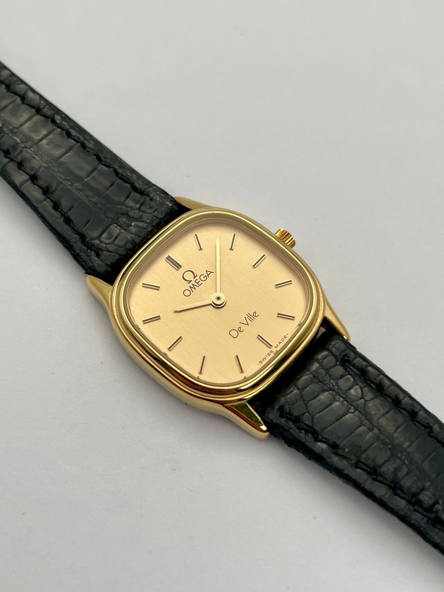 Omega De Ville vintage gold watch with a square case, champagne dial, and black leather strap, main view.