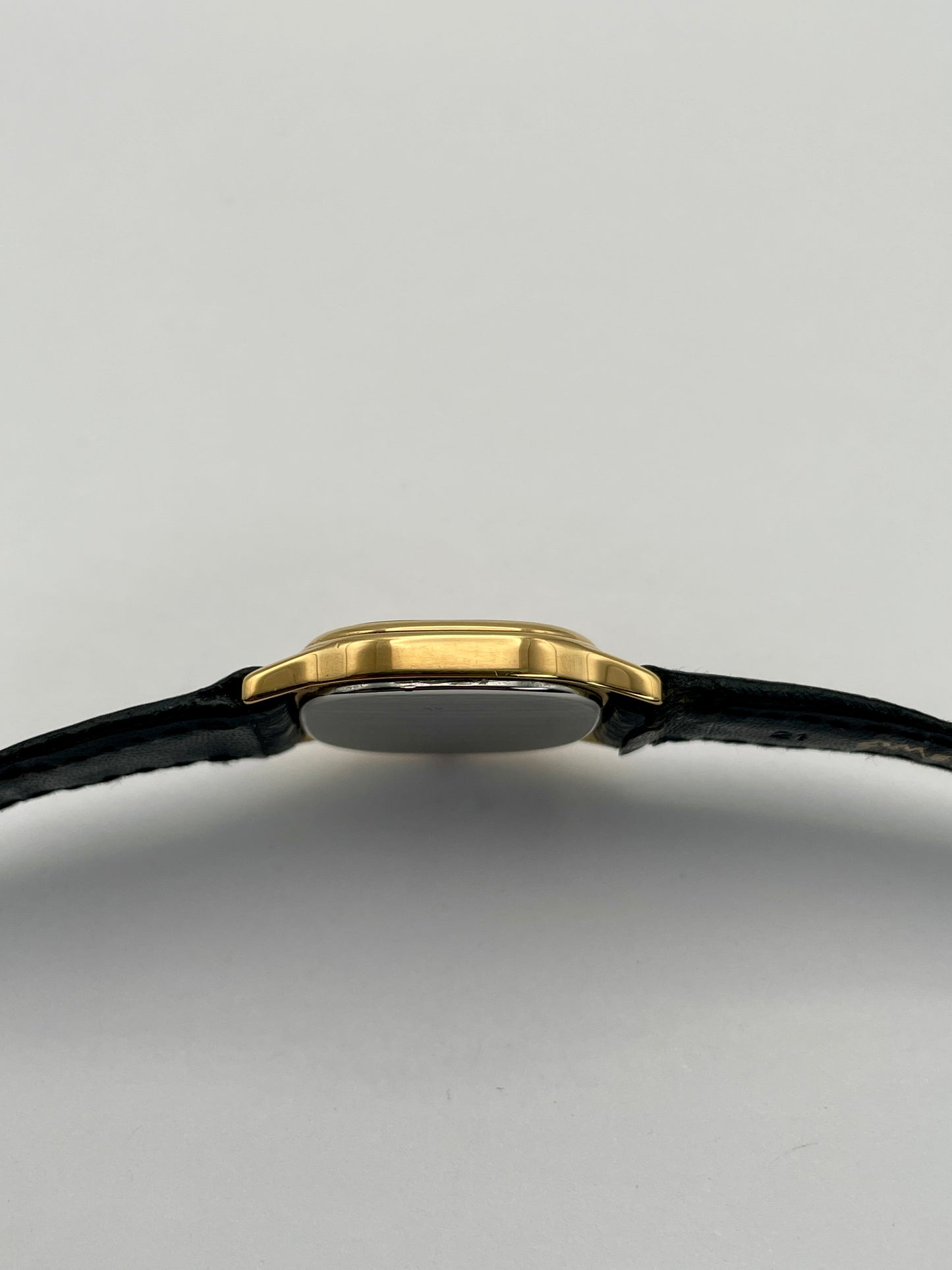 Side case view of Omega De Ville vintage gold watch with a slim gold case and black leather strap.