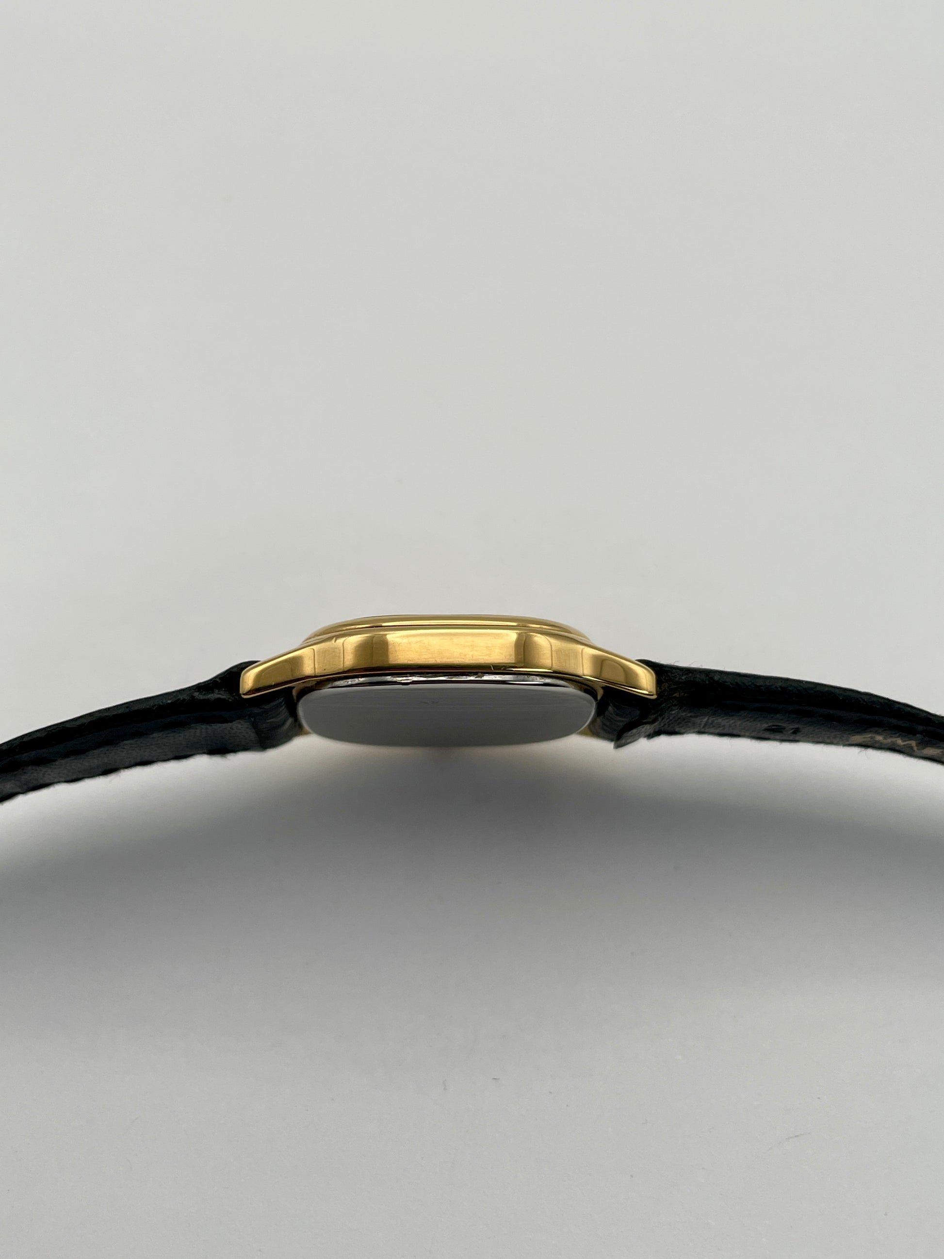 Side case view of Omega De Ville vintage gold watch with a slim gold case and black leather strap.