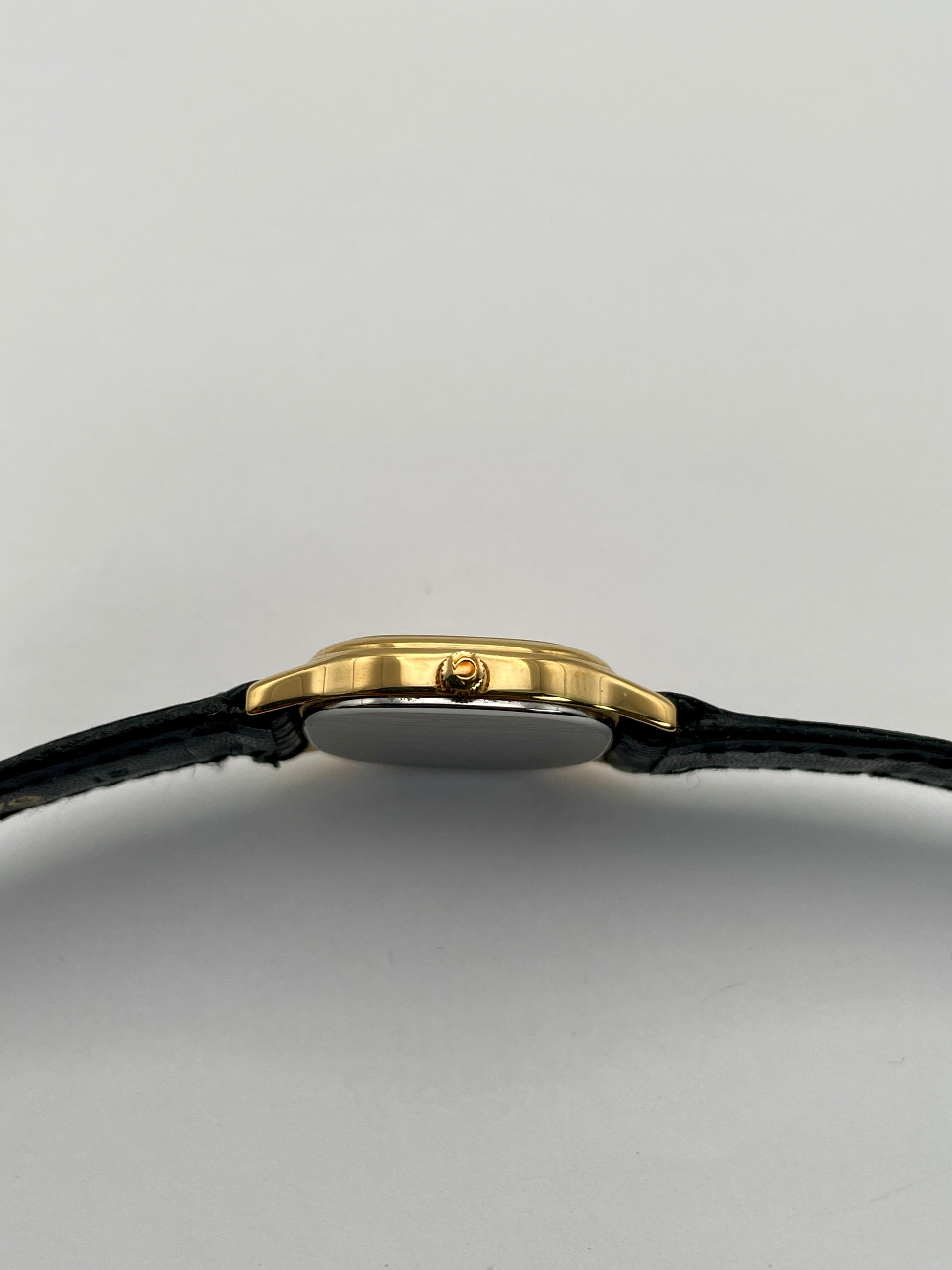 Side crown view of Omega De Ville vintage gold watch showing the gold crown and square case with black leather strap.