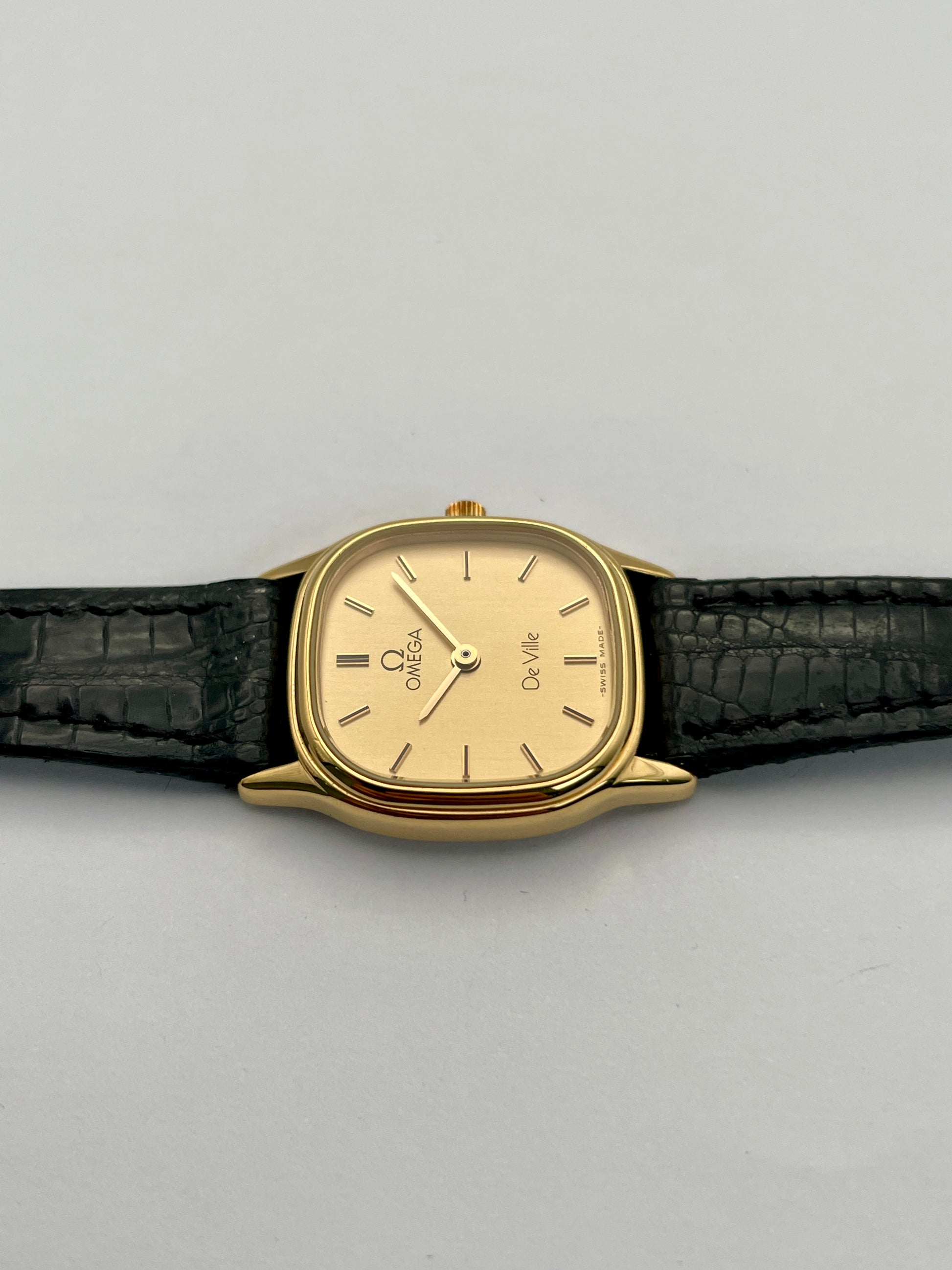 Top side case view of Omega De Ville vintage gold watch showing the slim gold case and black leather strap.