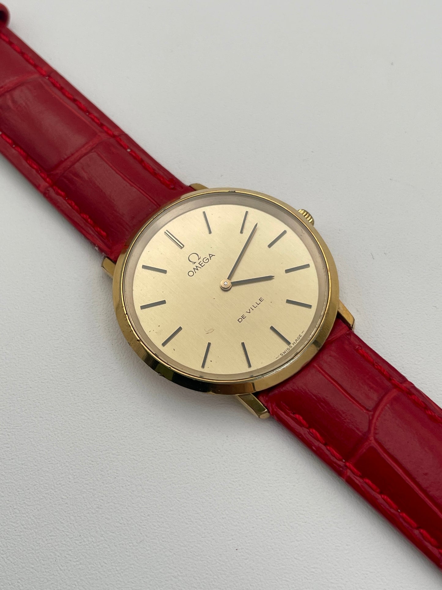 Omega De Ville Ref. 111.0144 gold watch with red strap, flatlay view.