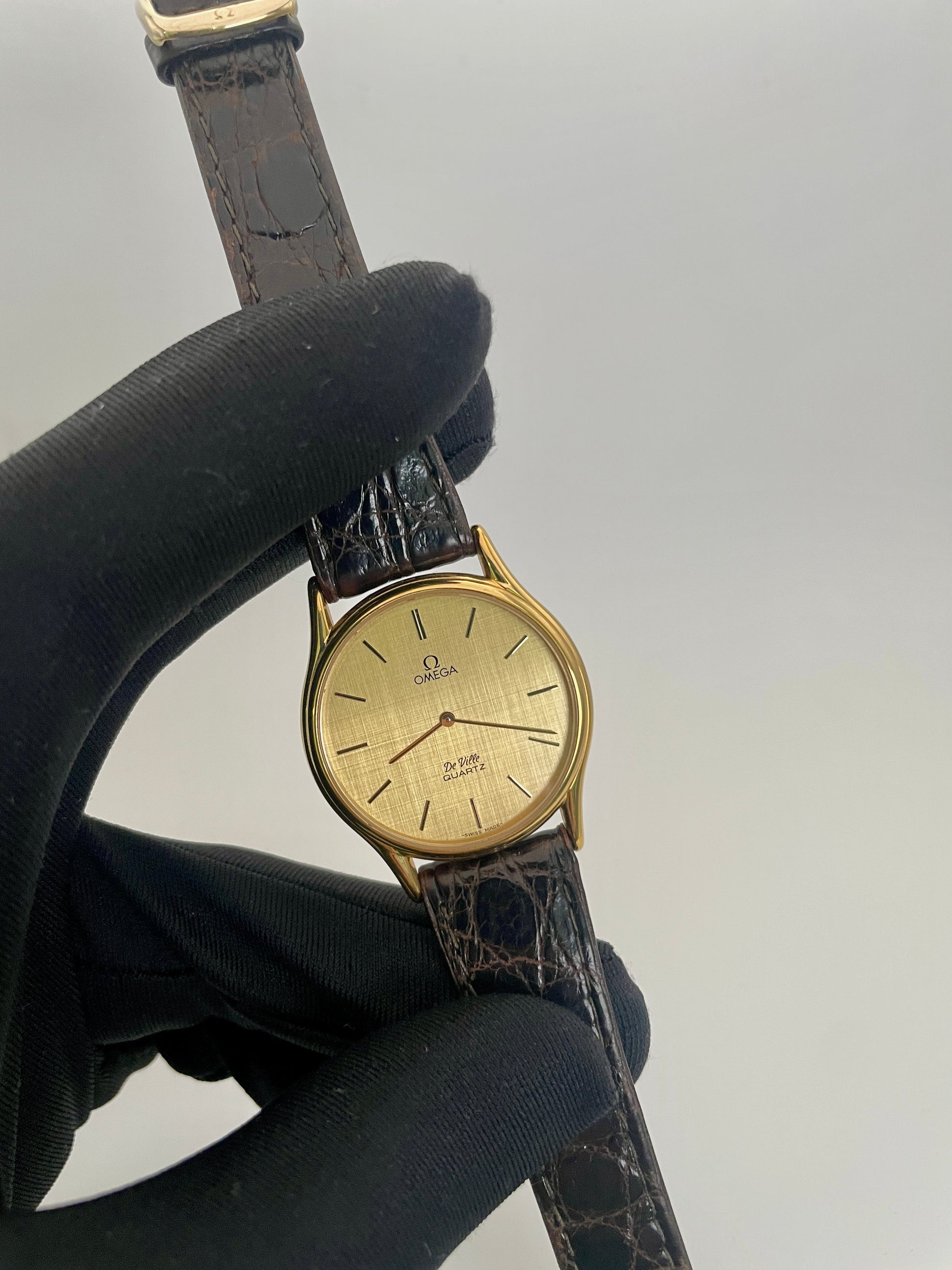 Close up view of Omega Deville Classic Ref 191.0130 gold watch with a round case, gold dial, and black leather strap.