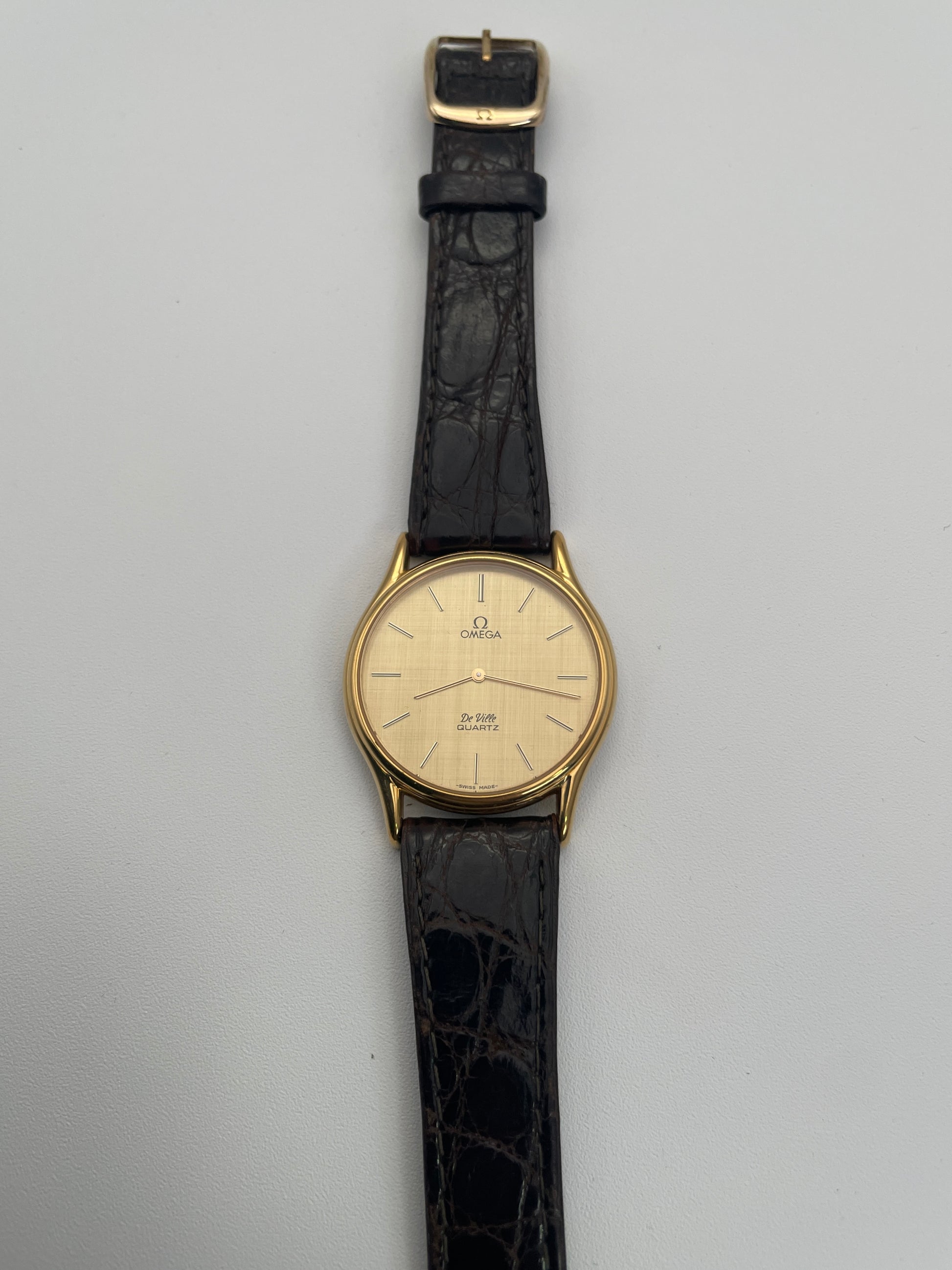 Front view of Omega Deville Classic Ref 191.0130 gold watch with a round case, gold dial, and black leather strap.