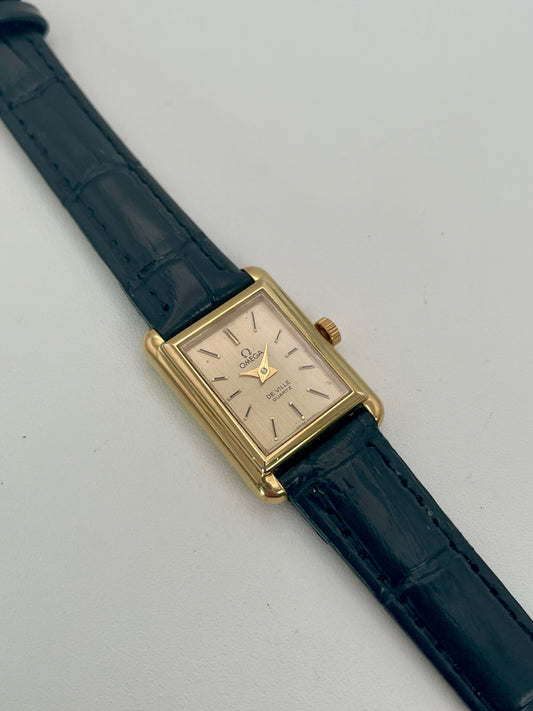 Front view of the Omega De Ville Tank Vintage Women's Watch in a gold rectangular case with champagne dial and dark navy leather strap.

