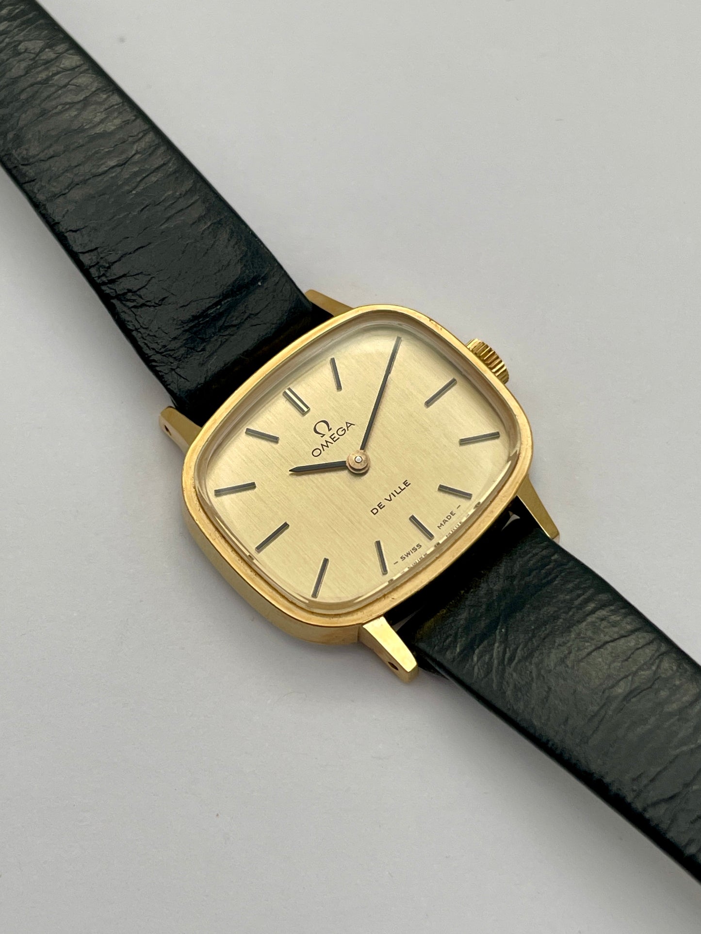 Omega De Ville TV Dial watch with a gold-tone square case and black leather strap.