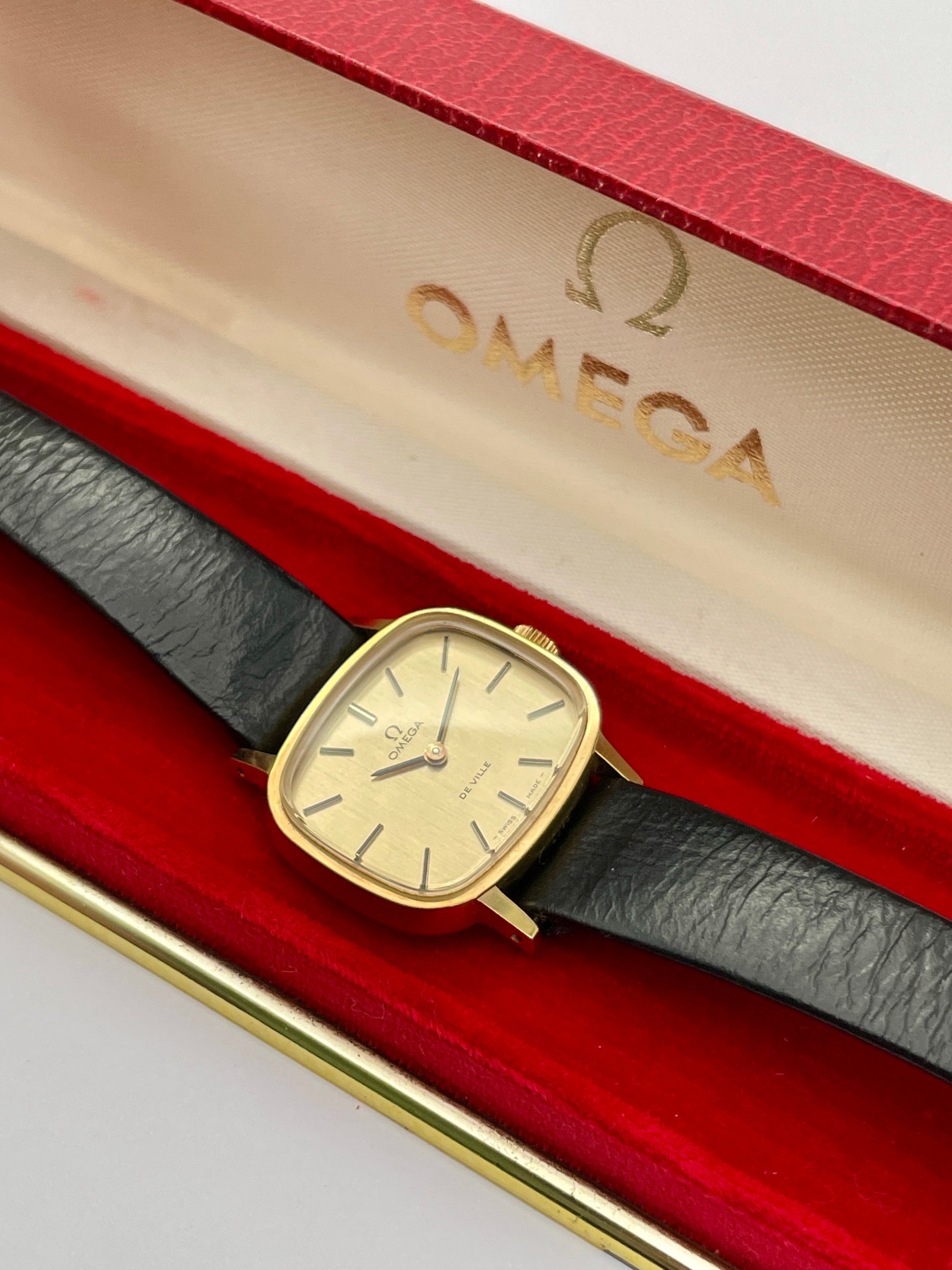 Omega De Ville TV Dial watch in its original red Omega box with a gold-tone square case and black leather strap.