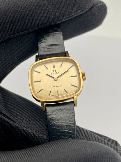 Close-up view of Omega De Ville TV Dial watch with a gold-tone square case and black leather strap.