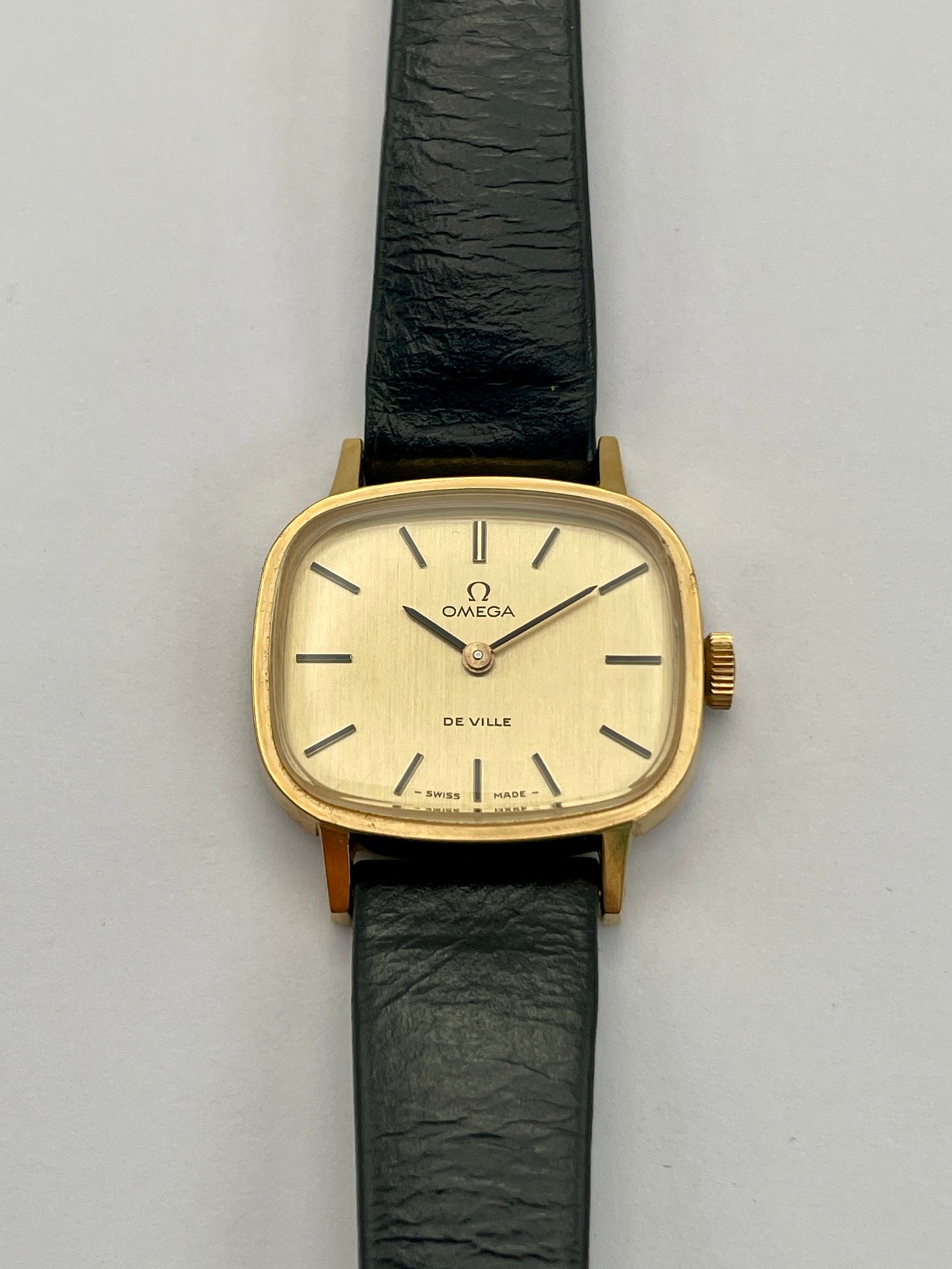 Front view of Omega De Ville TV Dial watch featuring a gold-tone square case and black leather strap.