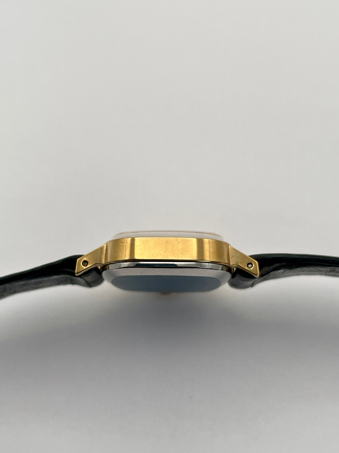 Side view of Omega De Ville TV Dial watch highlighting the gold-tone square case and black leather strap.