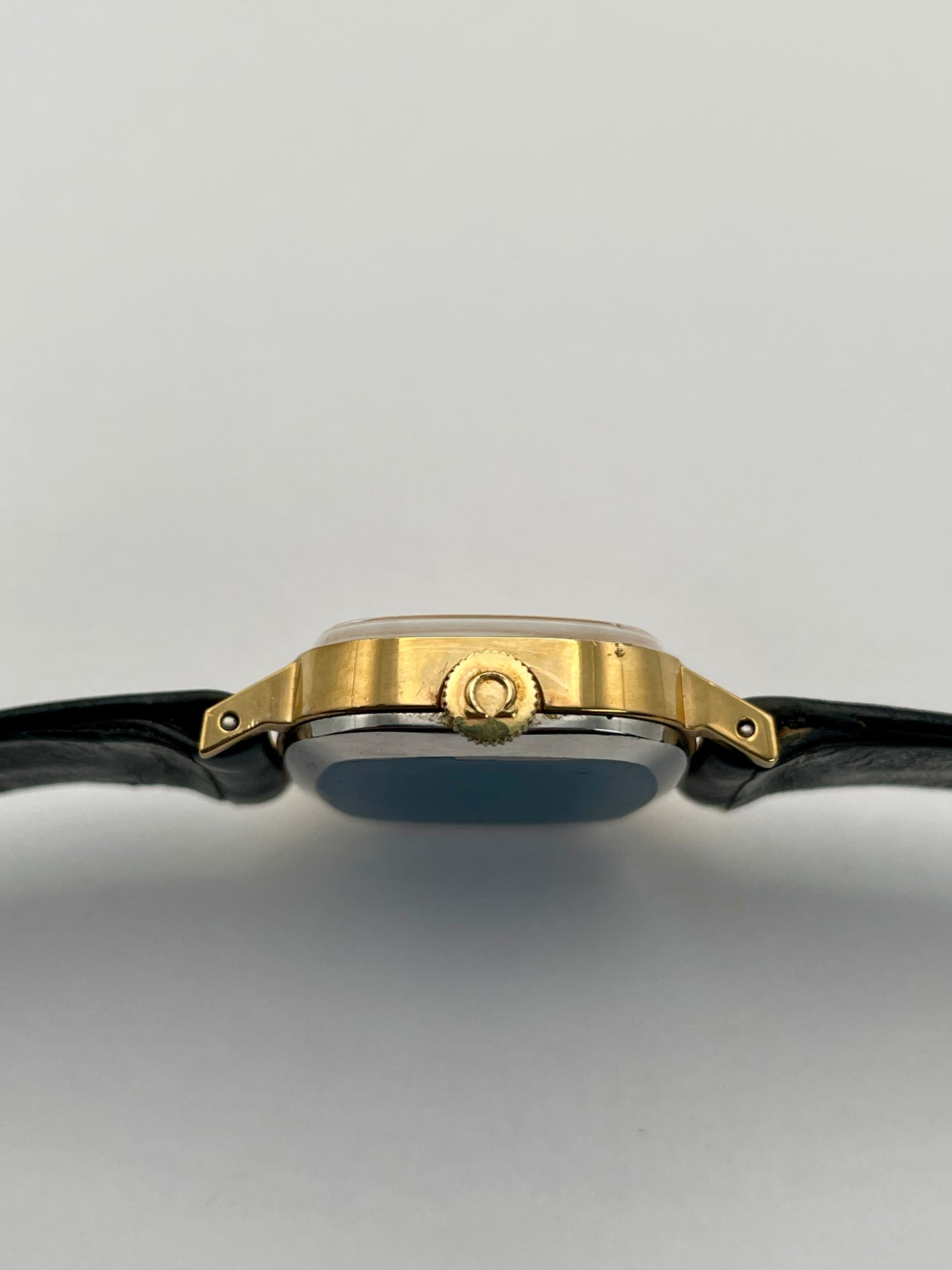 Side crown view of Omega De Ville TV Dial watch highlighting the gold-tone square case and black leather strap.