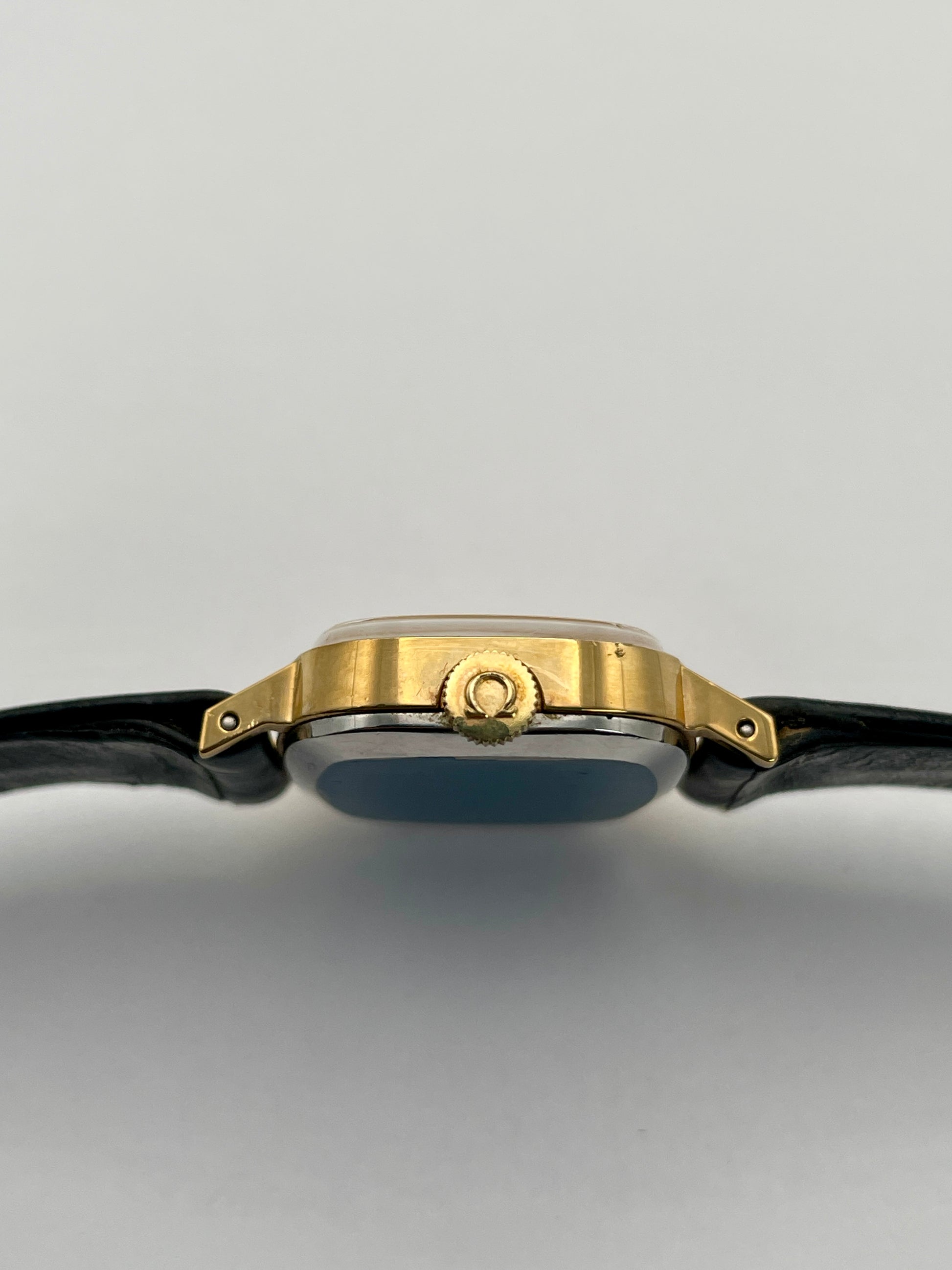 Side crown view of Omega De Ville TV Dial watch highlighting the gold-tone square case and black leather strap.