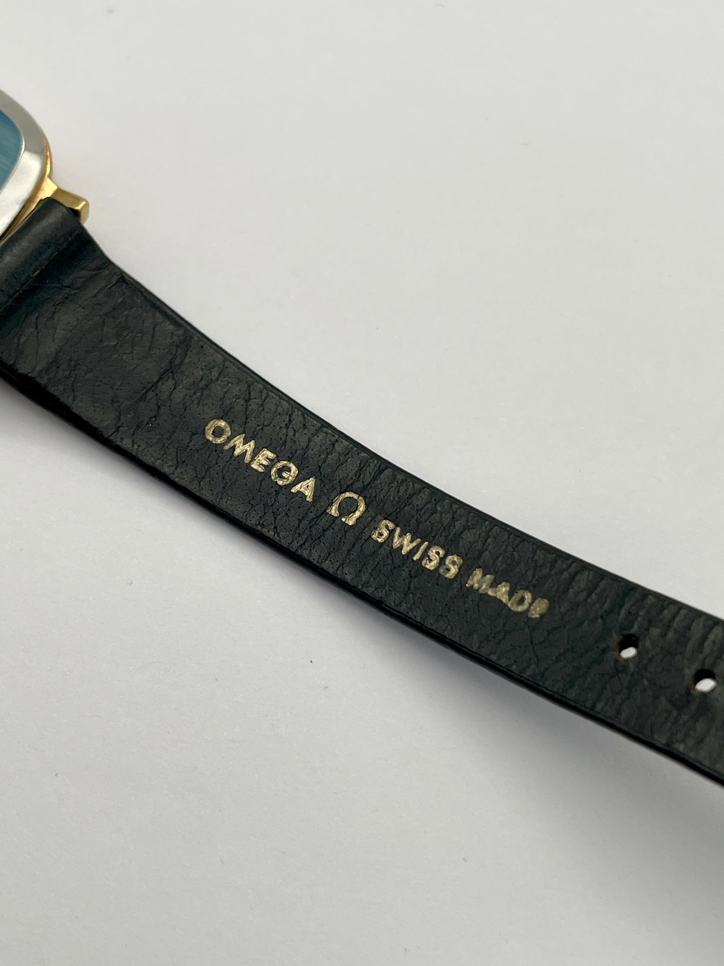 Close-up view of Omega De Ville TV Dial strap showcasing original Omega strap and branding, watch with a gold-tone square case and black leather strap.