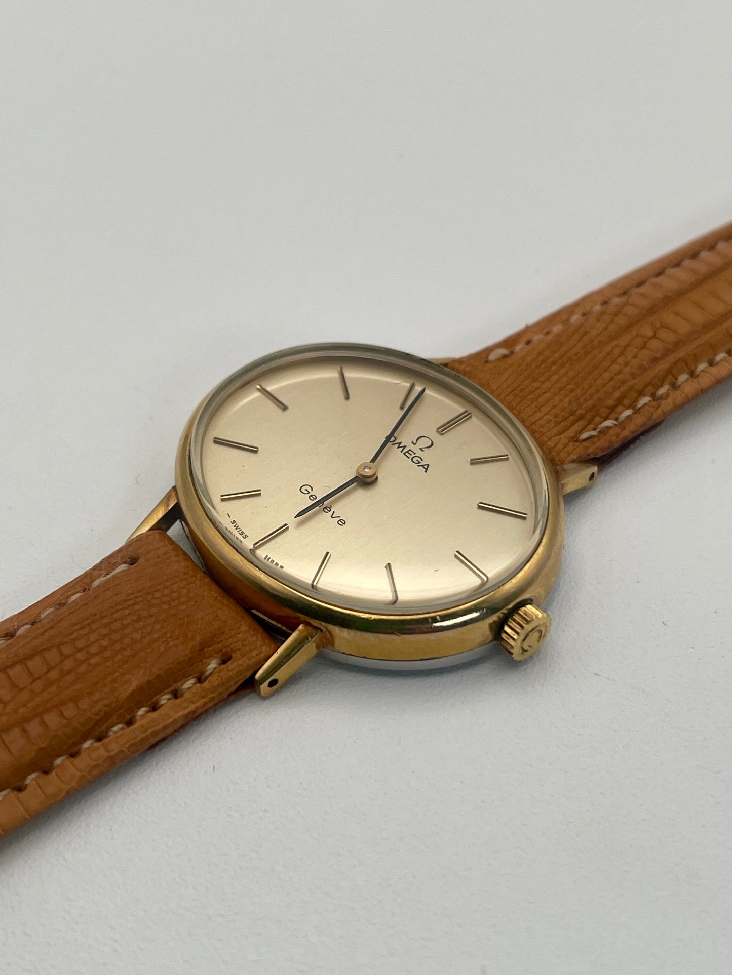 Diagonal view of Omega Genève Ladies Watch with oval gold case and tan leather strap.