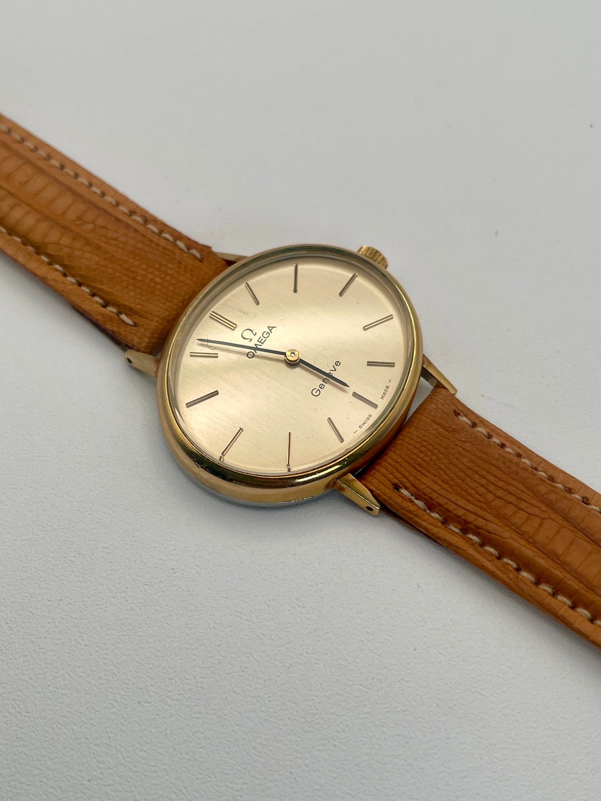 Flatlay view of Omega Genève Ladies Watch with oval gold case and tan leather strap.