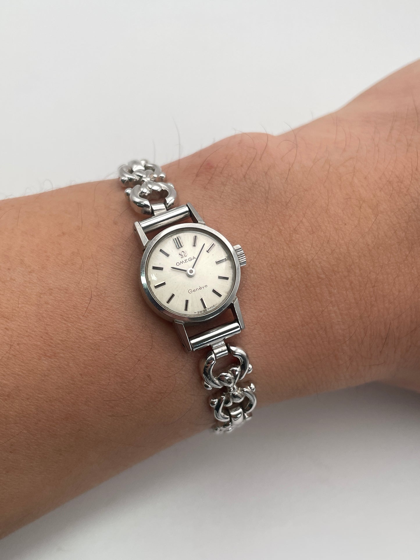 Wrist shot of Omega Genève ladies watch in silver-tone with a round case, silver dial, and intricate bracelet.