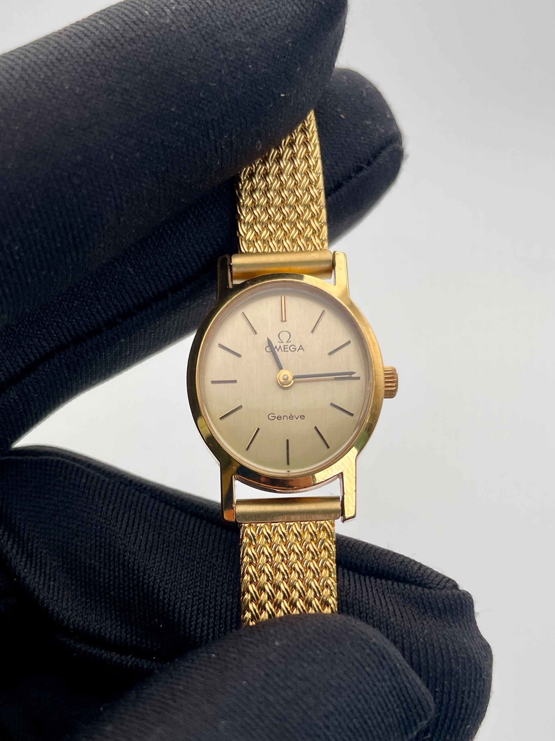 Omega Genève oval ladies watch in gold with a mesh bracelet, close-up view.
