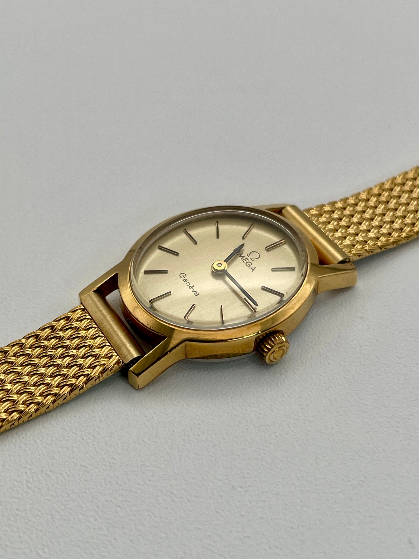 Omega Genève oval ladies watch in gold with a mesh bracelet, diagonal view.
