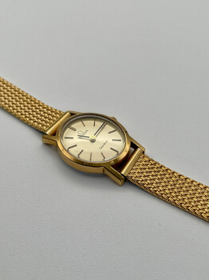 Omega Genève oval ladies watch in gold with a mesh bracelet, flatlay view.
