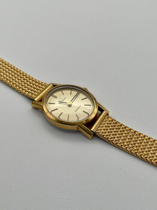 Omega Genève oval ladies watch in gold with a mesh bracelet, flatlay view.
