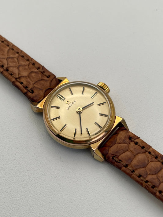 Photo of a vintage Omega ladies watch with gold bullhorn lugs, tan leather strap, and a gold-tone dial.
