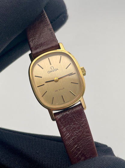 Handheld close-up of the Omega De Ville 511.0509 watch, showcasing the gold case, minimalist dial, and brown leather strap.