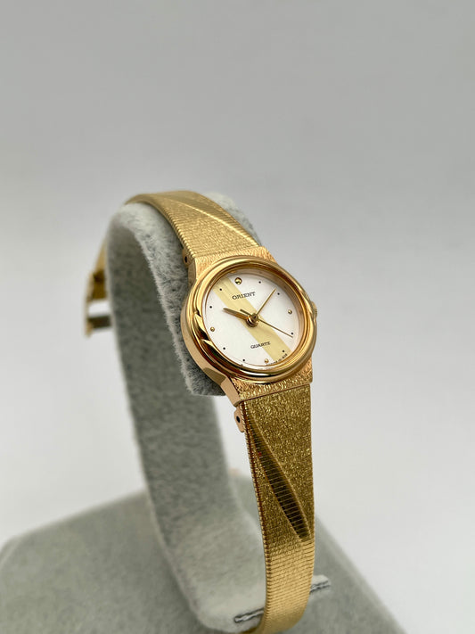 Display stand view of the Orient Vintage Women's Watch with its gold bracelet and minimalist dial.