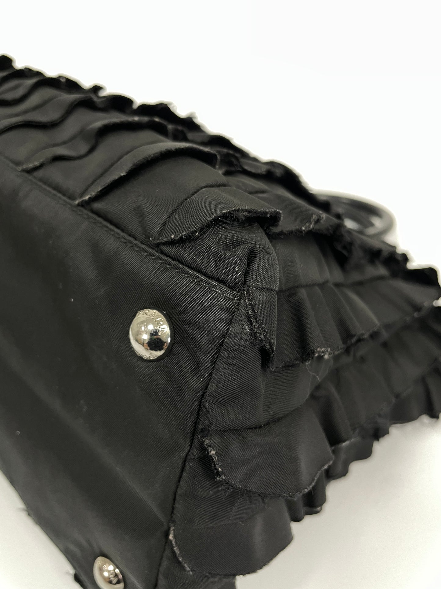 Close-up view of the corner of Prada Tessuto Ruffle Bag in black nylon, featuring protective silver-tone studs.