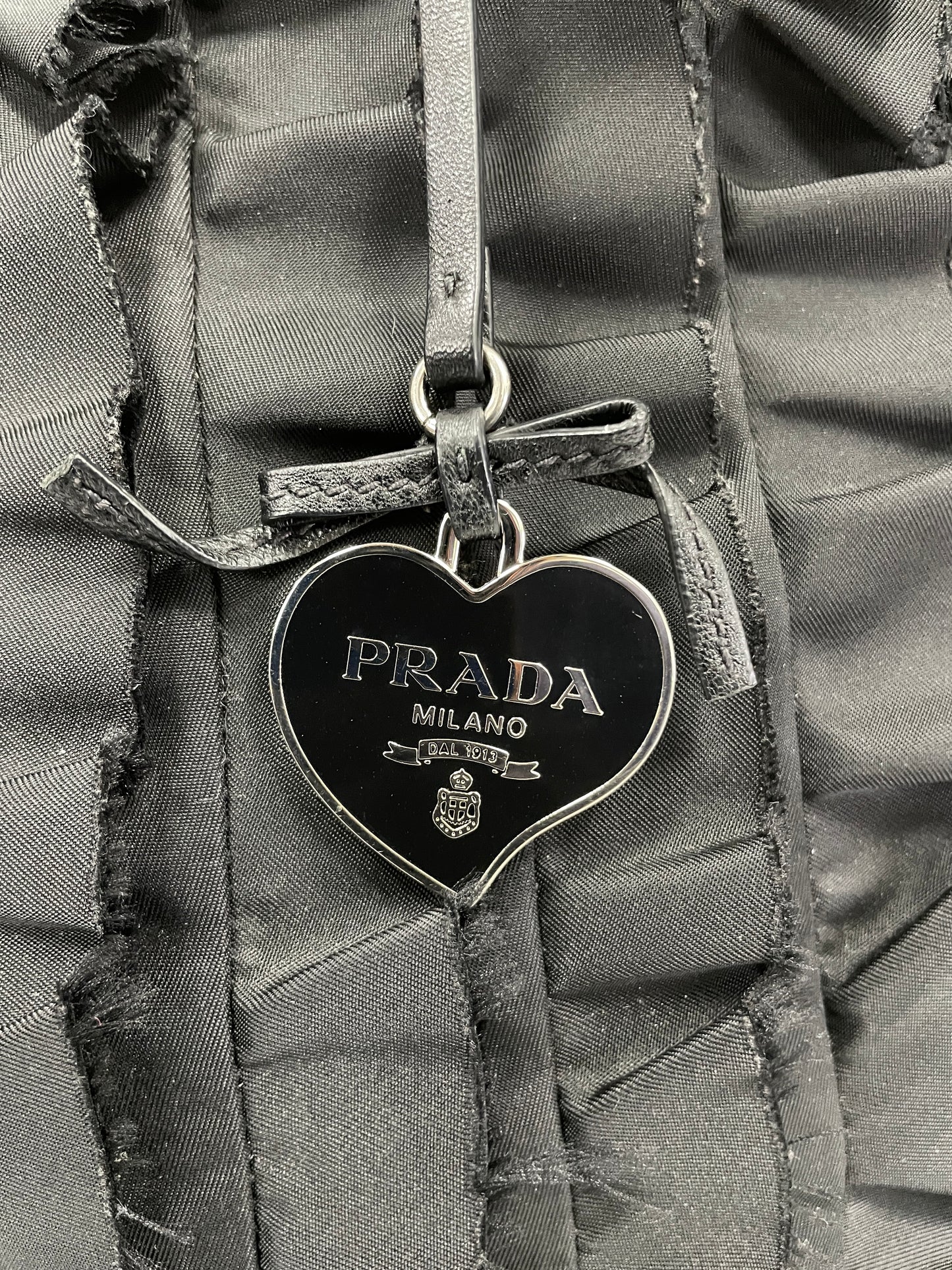 Close-up view of the Prada heart-shaped charm attached to the Tessuto Ruffle Bag in black nylon.