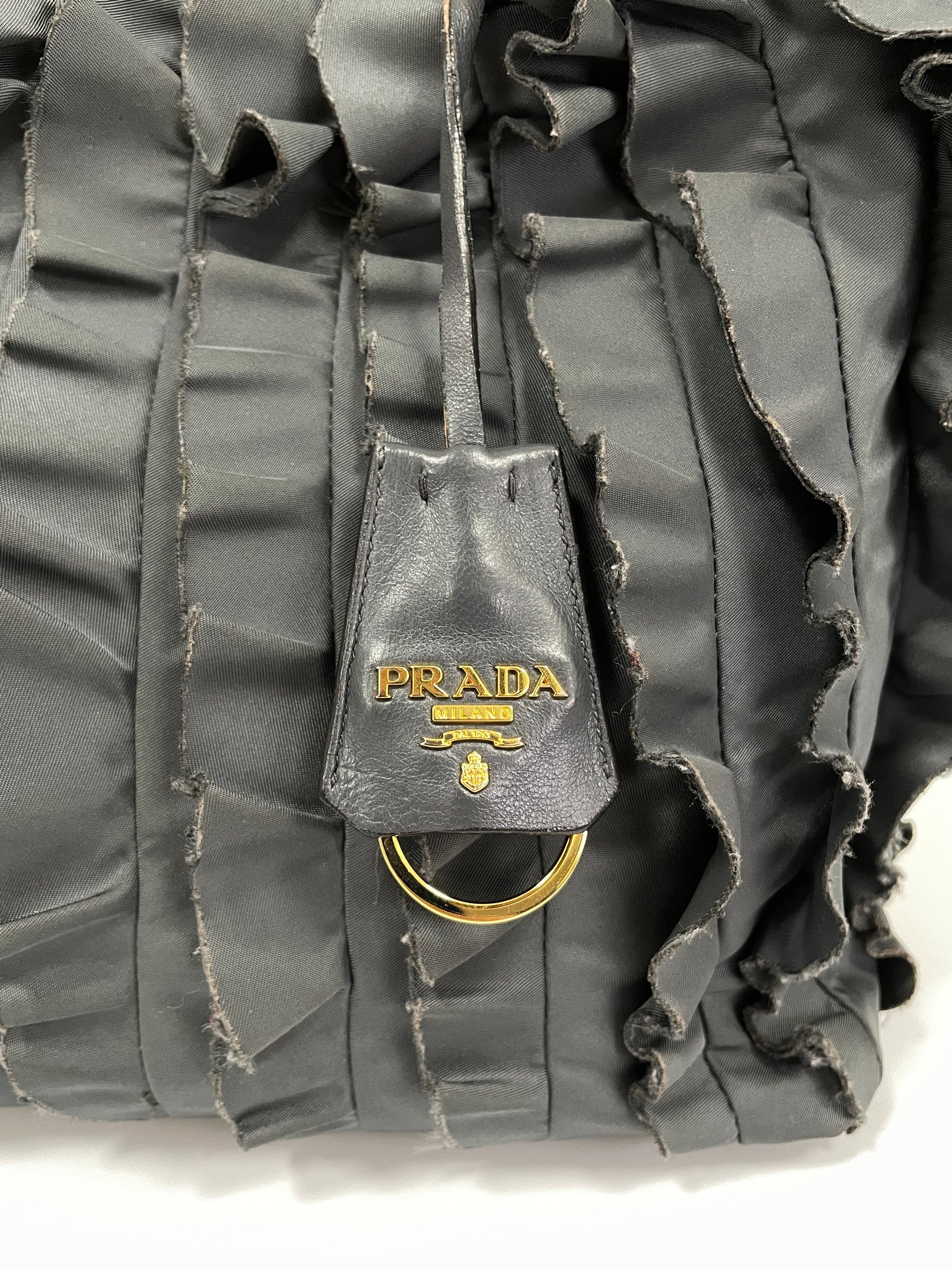 Detailed view of the Prada logo charm tag with gold-tone ring on the Prada Tessuto Ruffle Bag in grey nylon.