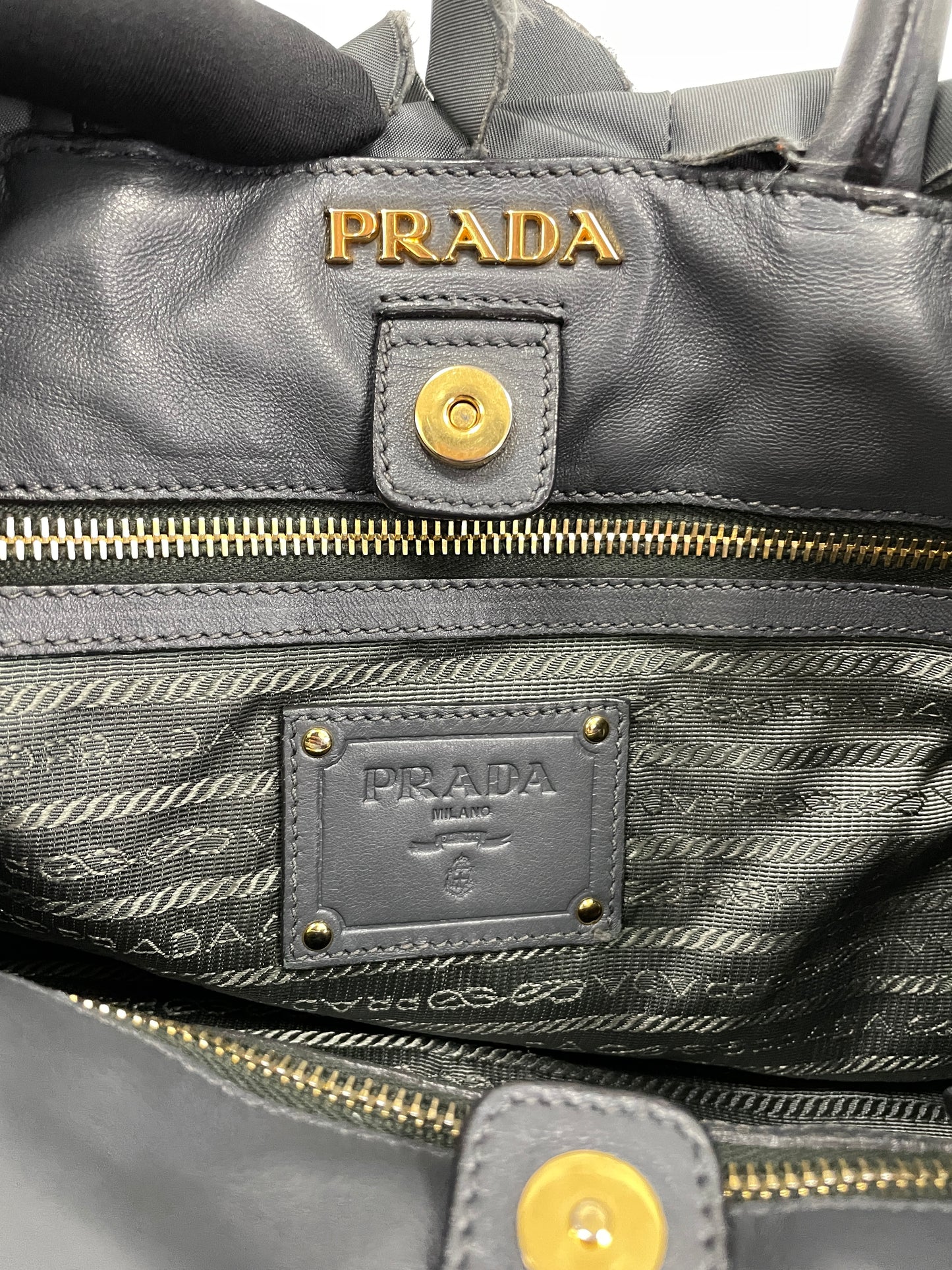 Close-up of Prada logo in gold-tone hardware inside the Tessuto Ruffle Bag in grey nylon.