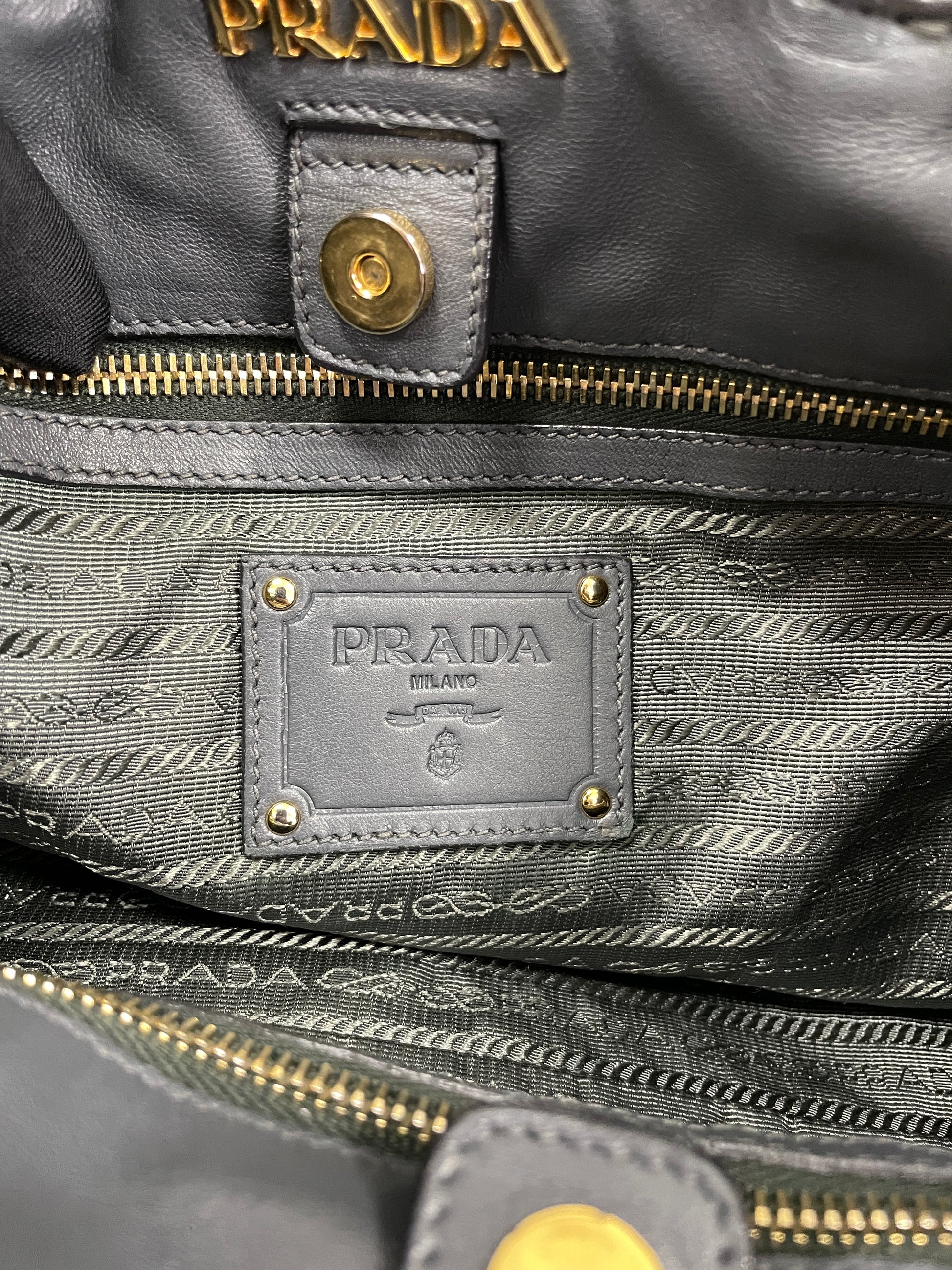 Close-up of Prada logo in gold-tone hardware inside the Tessuto Ruffle Bag in grey nylon.