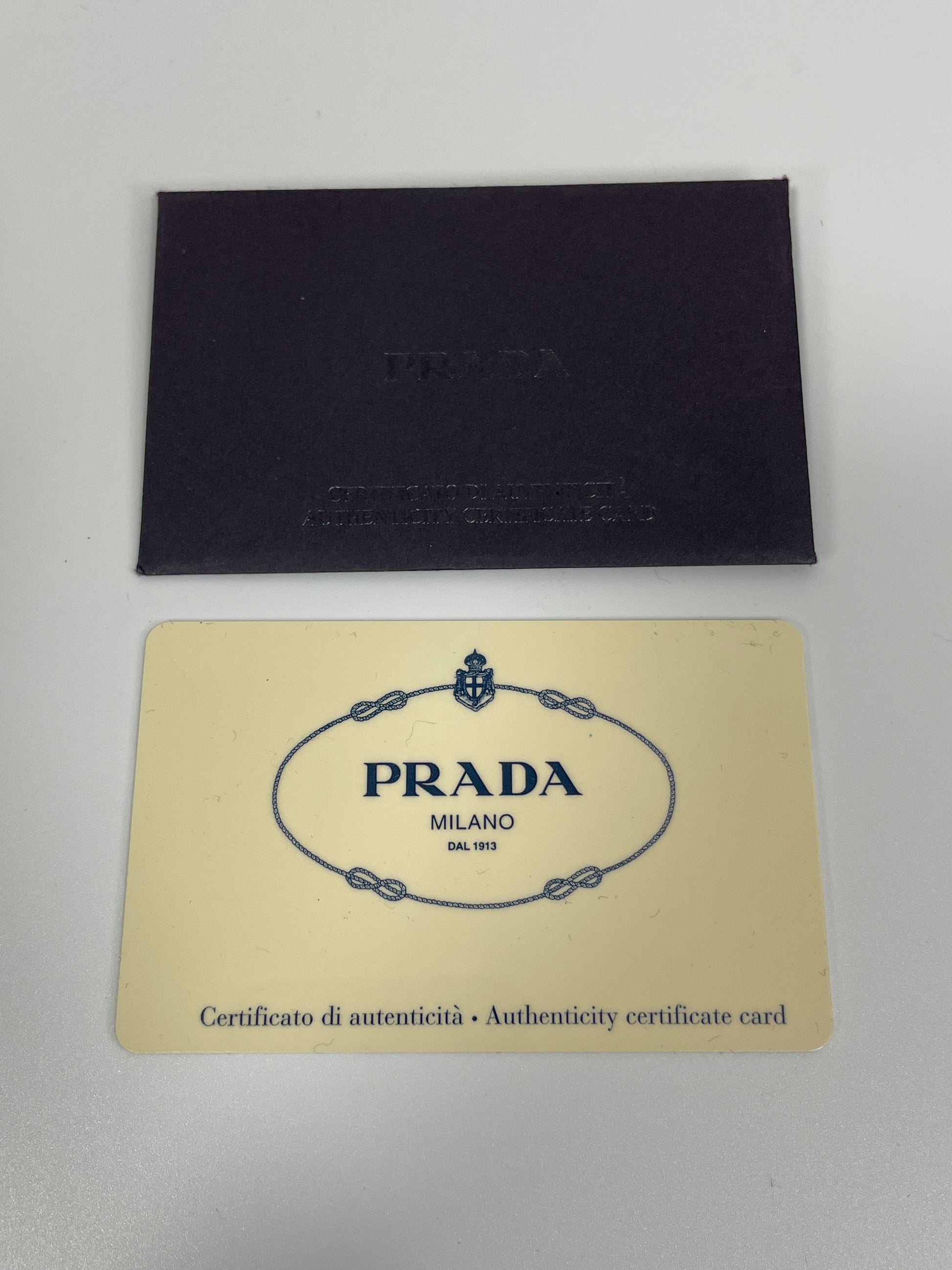 Prada authenticity card and certificate displayed with the Prada Tessuto Spazzolato bag in indigo prune nylon.