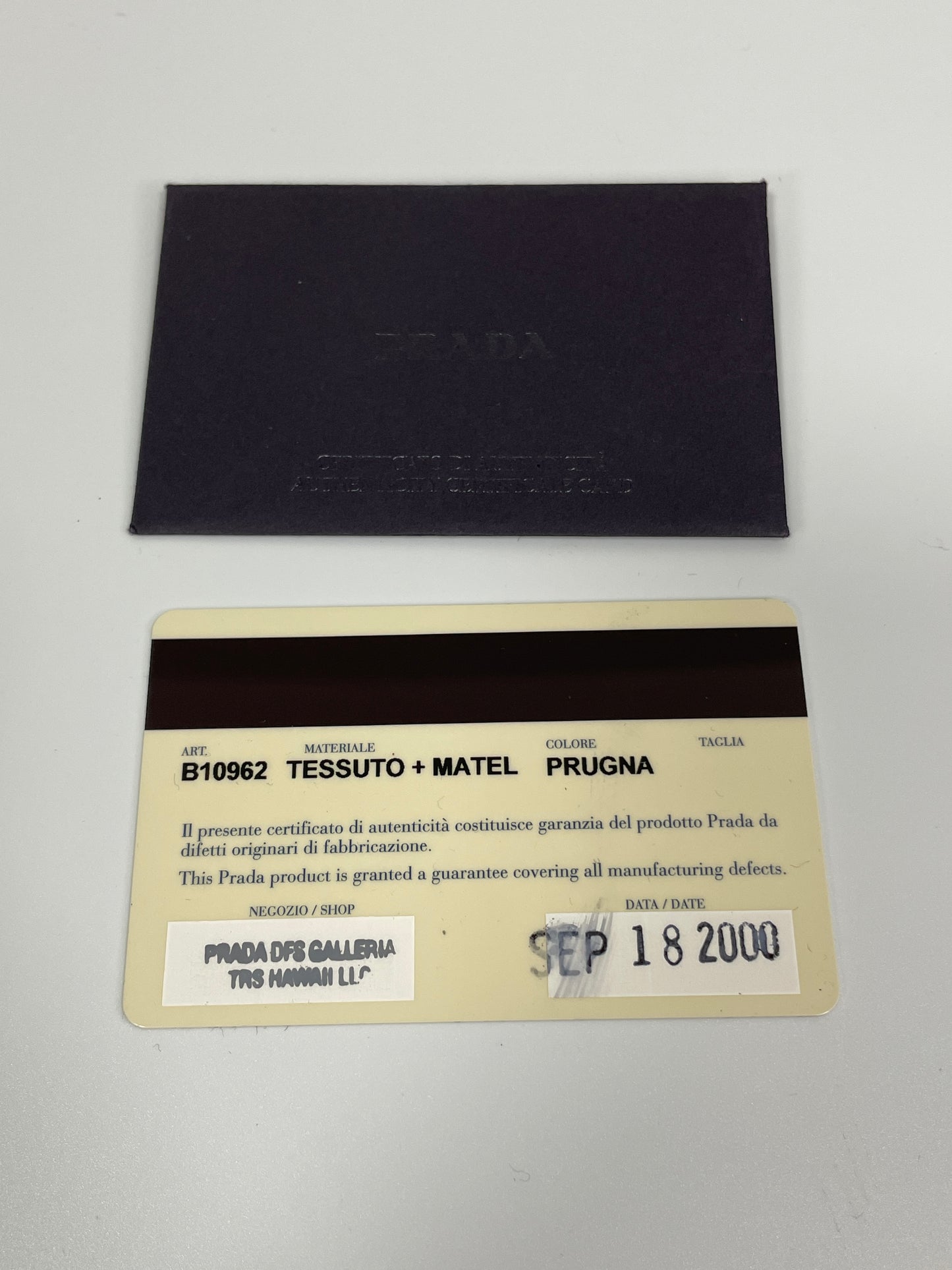 Prada authenticity card and certificate displayed with the Prada Tessuto Spazzolato bag in indigo prune nylon.