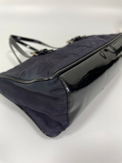 Close up corner bottom view of a Prada Tessuto Spazzolato bag in indigo prune nylon featuring a glossy leather bottom.