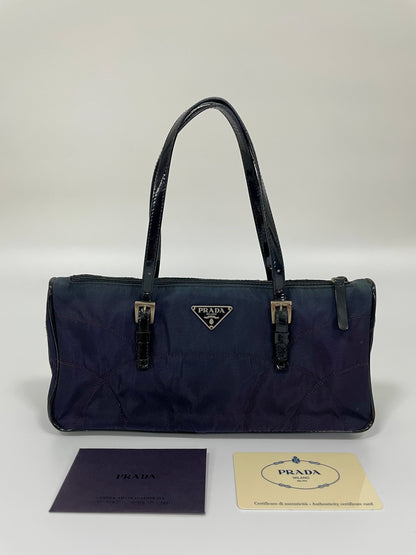 Front view of a Prada Tessuto Spazzolato bag in indigo prune nylon with leather handles and signature Prada triangle logo, displayed with authenticity cards.