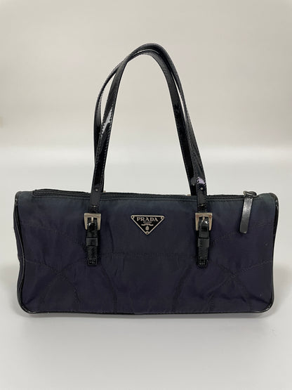 Front view of a Prada Tessuto Spazzolato bag in indigo prune nylon with patent leather handles and signature Prada triangle logo.