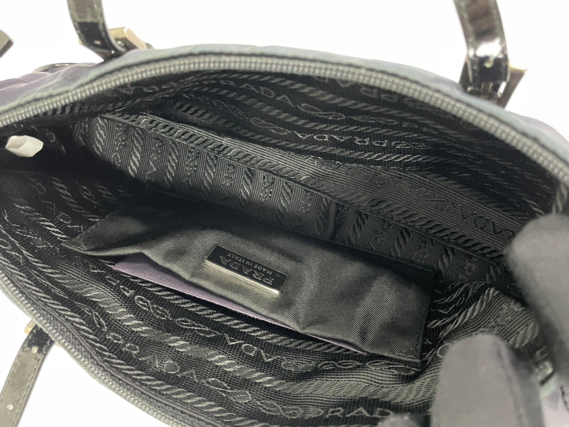 Interior view of a Prada Tessuto Spazzolato bag in indigo prune nylon showcasing the spacious black fabric lining and the authenticity card.