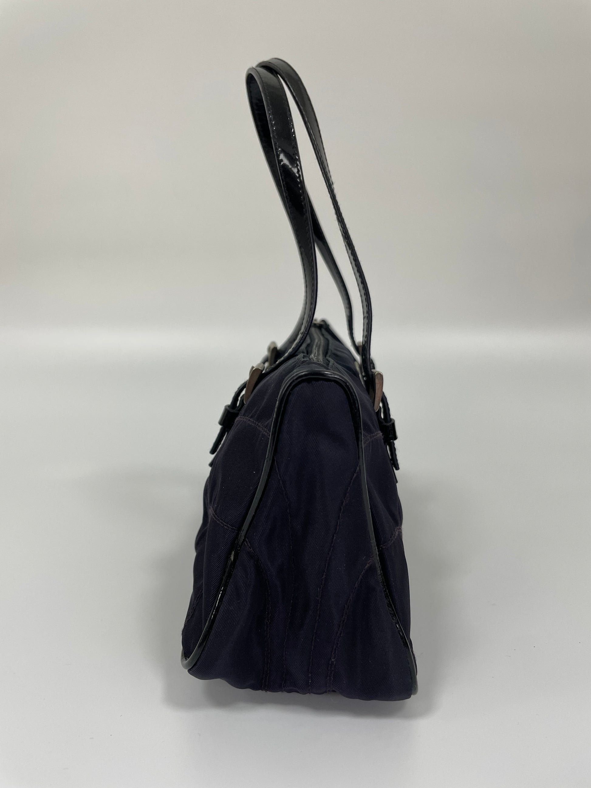 Side view of a Prada Tessuto Spazzolato bag in indigo prune nylon showcasing its slim profile and leather handles.